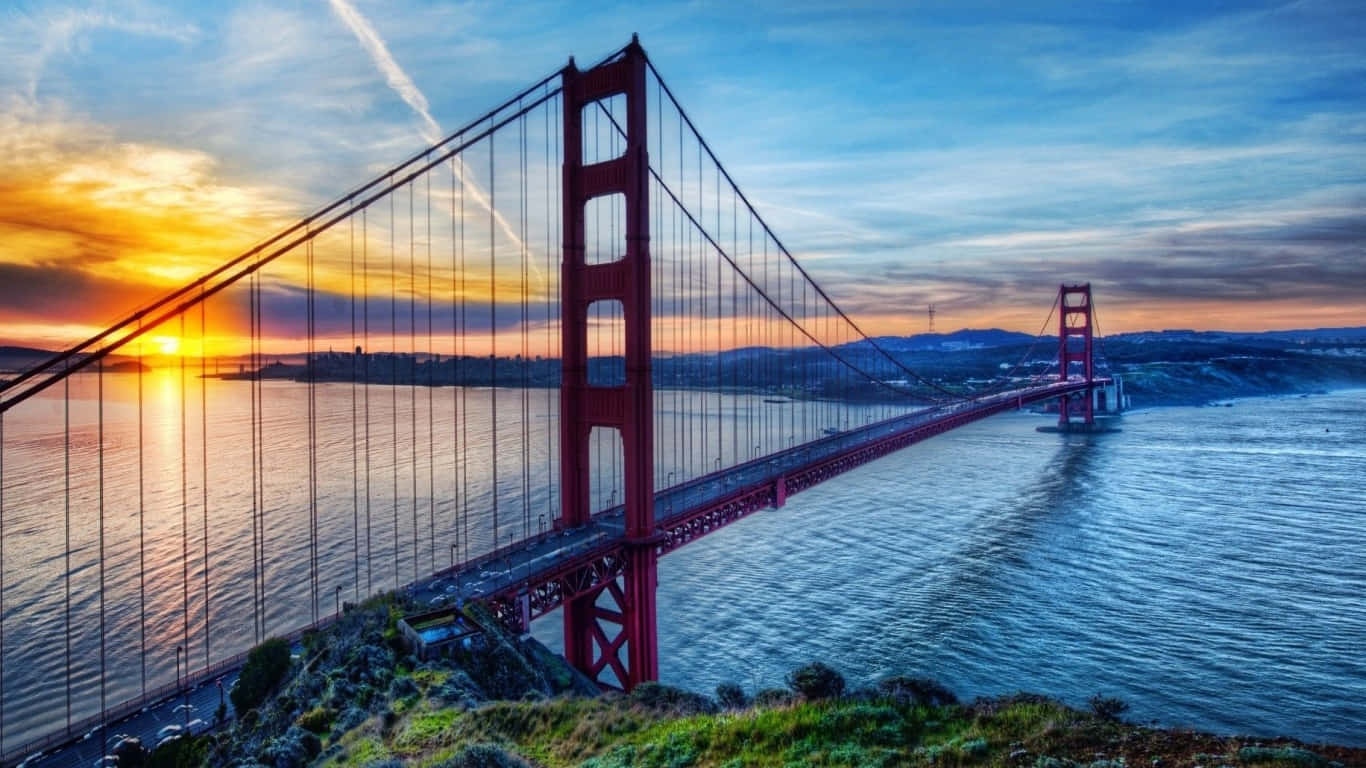 1366x768 San Francisco 桌布 壁紙 — 金門大橋在平靜的水面上，以火熱的日落色調發光，伴隨著戲劇性的雲彩和遠山。