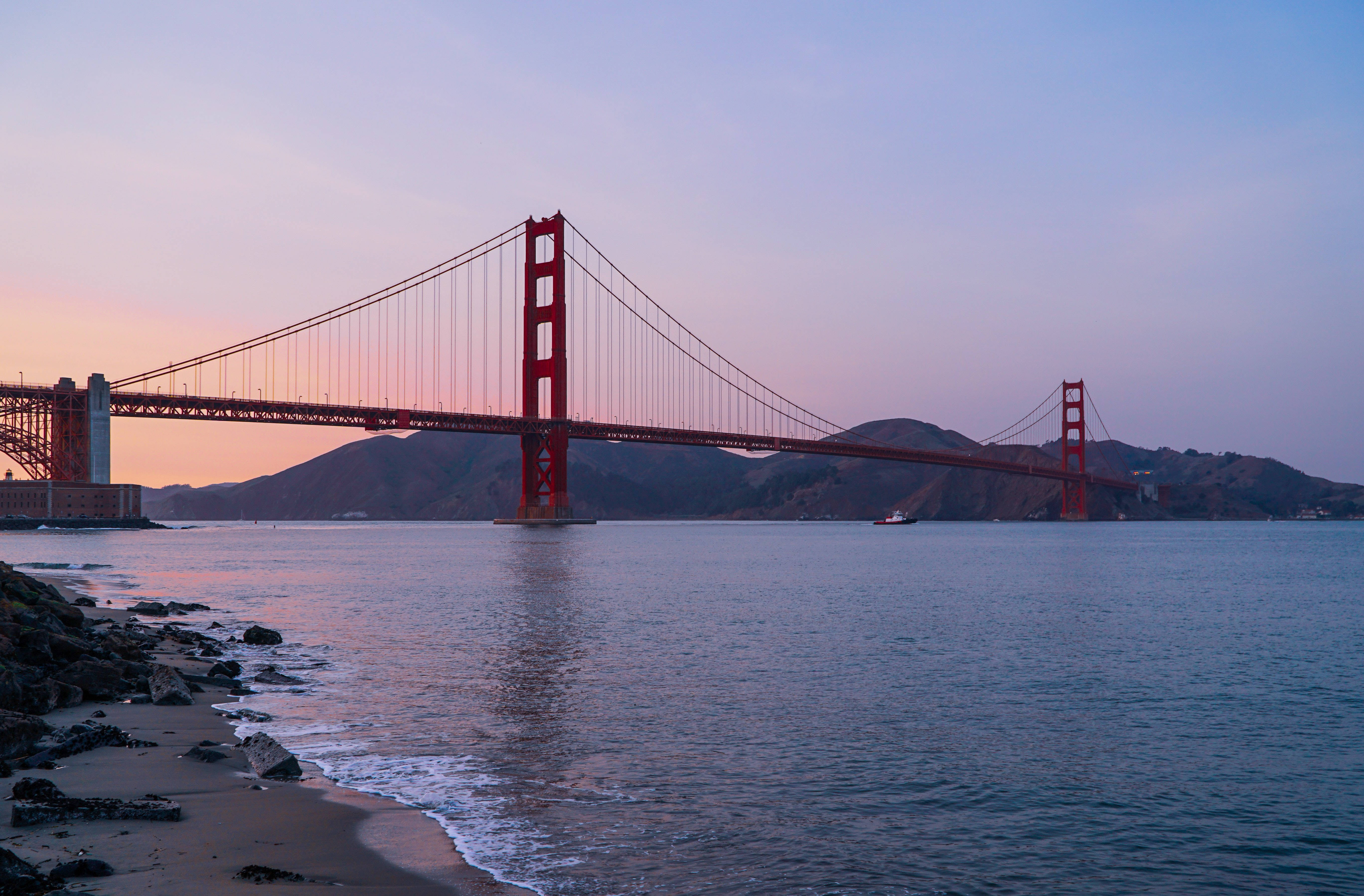 San Francisco 桌布 壁紙 — 金門大橋在暮色中閃耀，其倒影在岩石海岸線旁的平靜水面上舞動。