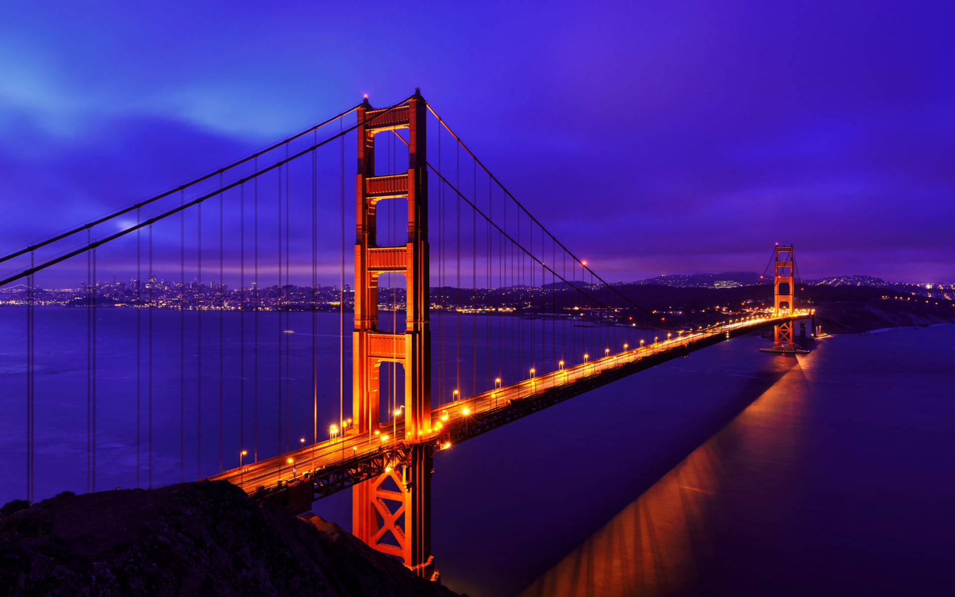 San Francisco HD 桌布 壁紙 — 金門大橋在深紫色暮色天空下溫暖地發光，城市燈光在海灣對岸閃爍。