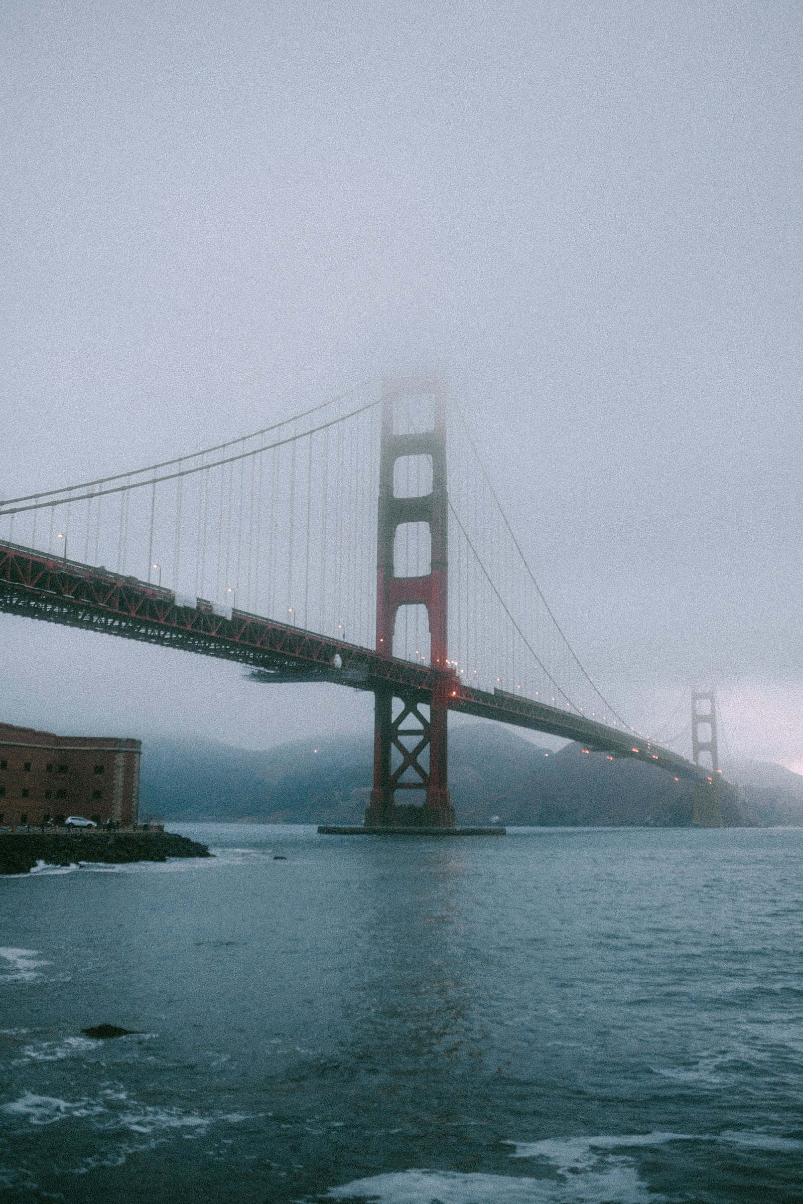 San Francisco Fog 桌布 壁紙 — 金門大橋在濃霧中浮現，橫跨平靜的海灣，呈現柔和的灰色和紅色色調。