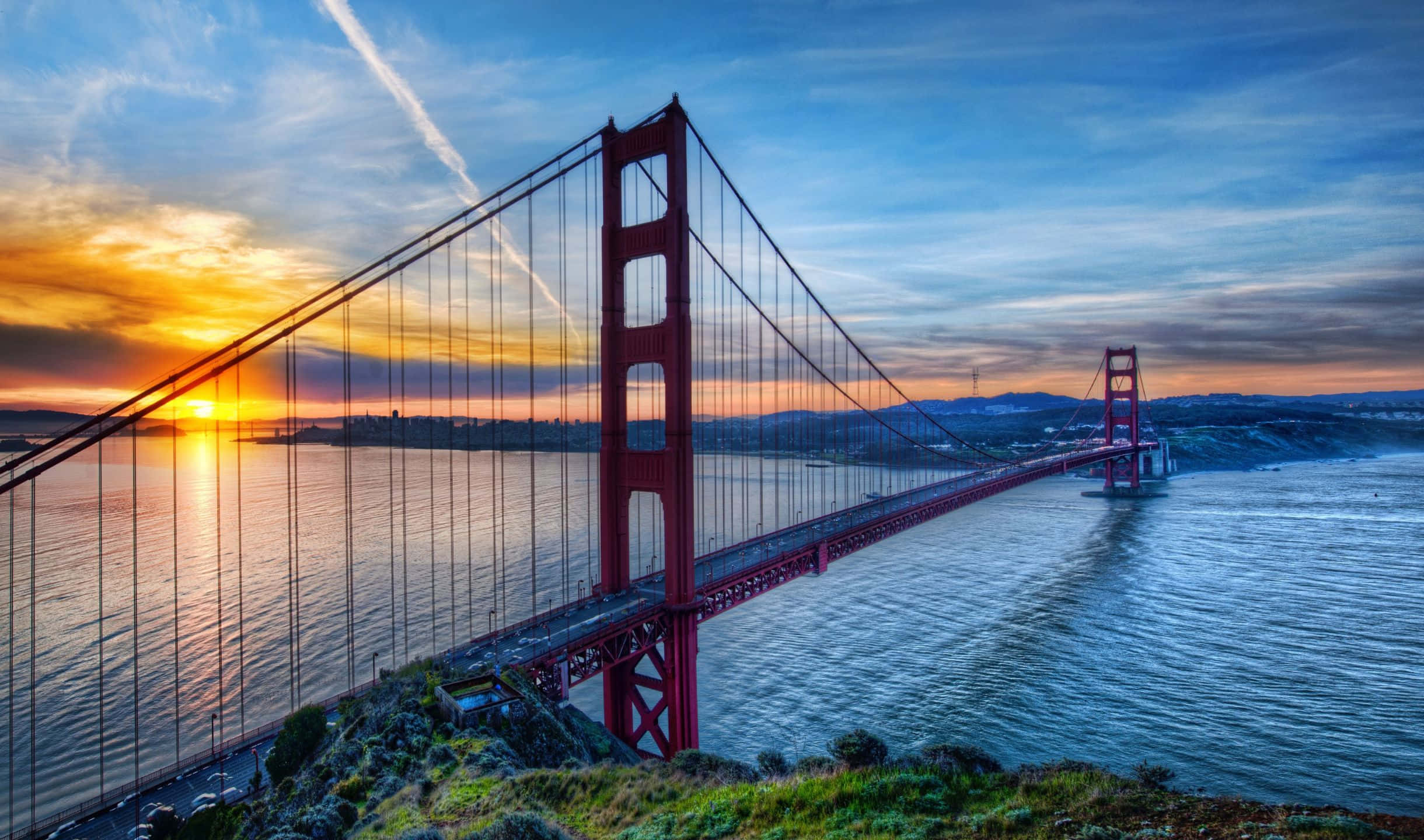 2440x1440 San Francisco 桌布 壁紙 — 金門大橋在火紅的日落色調中閃耀，橫跨在平靜的水面上，天空佈滿條紋雲彩。
