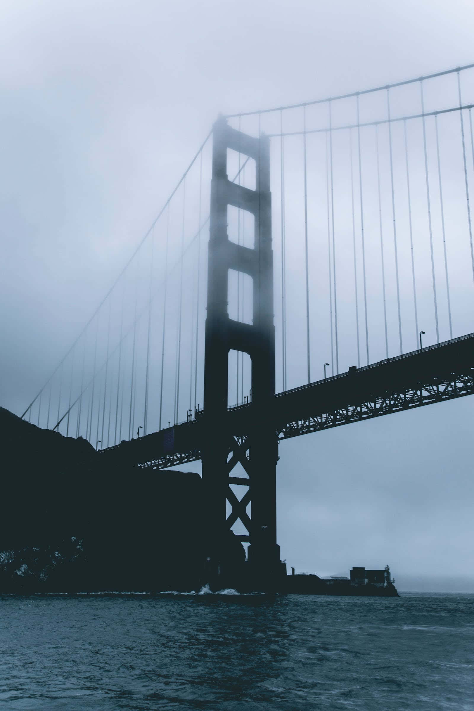 San Francisco Fog 桌布 壁紙 — 金門大橋在灰色天空下，聳立於暗黑水面上，呈現迷霧般的剪影。