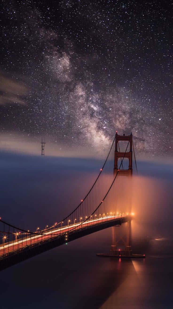 bridge 桌布 壁紙 — 金門大橋在繁星點點的夜空下溫暖地發光，銀河在其上方拱起。