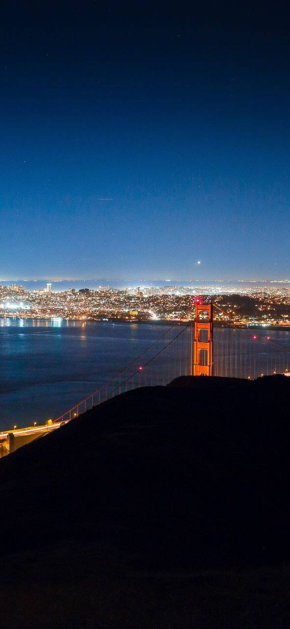 san francisco iPhone 桌布 壁紙 — 金門大橋在繁星點點的夜空下發出橙色光芒，城市燈光在海灣下方閃爍。