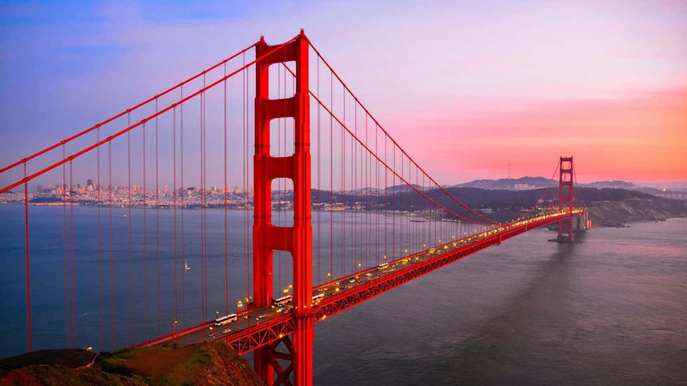 1366x768 San Francisco 桌布 壁紙 — 金門大橋在舊金山灣上空粉紅與藍色的日落天空映襯下發出紅光，遠處城市燈光閃爍。
