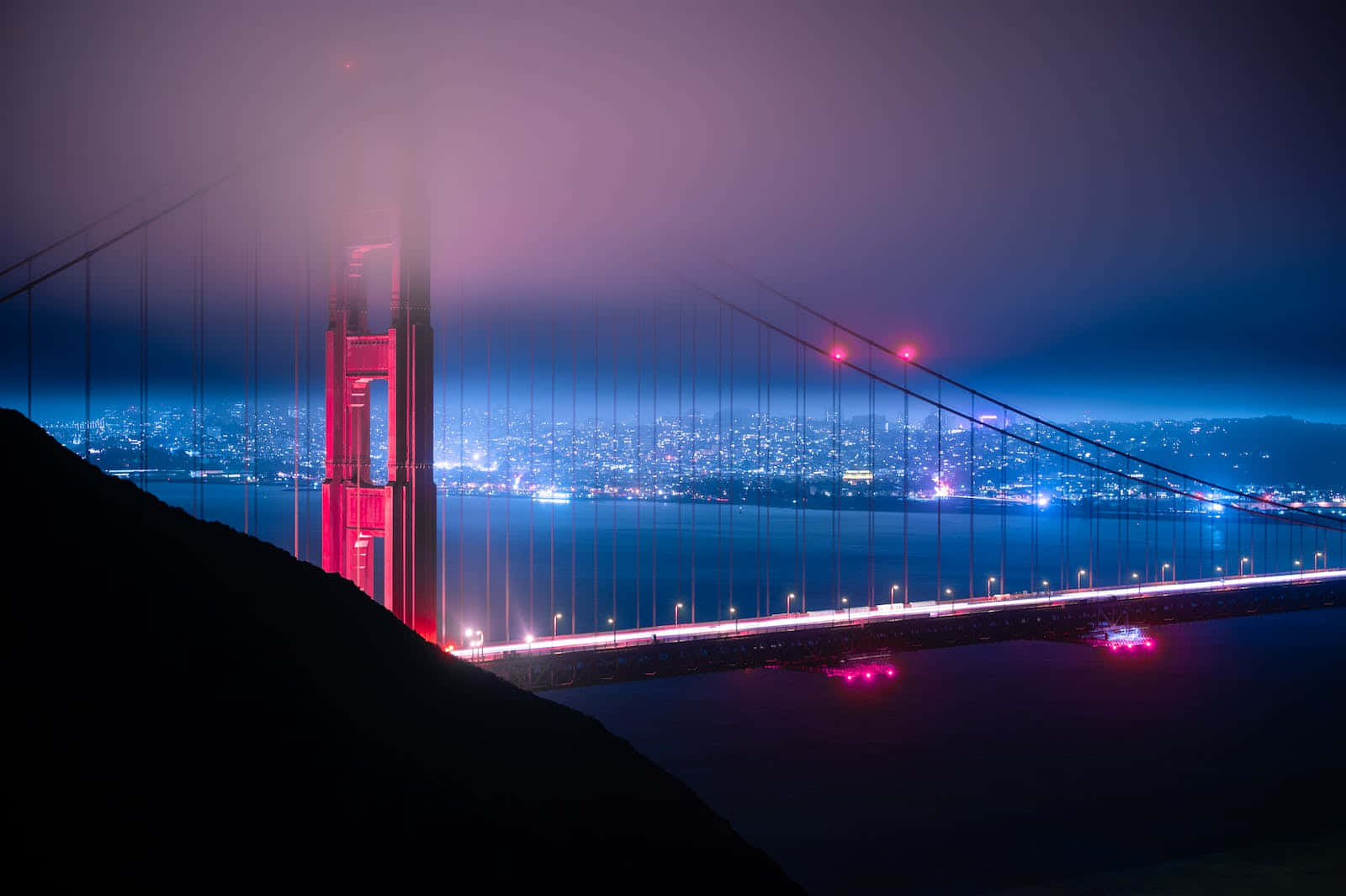San Francisco Fog 桌布 壁紙 — 金門大橋在薄霧中泛著紅光，城市燈光在深藍色夜空下閃爍。