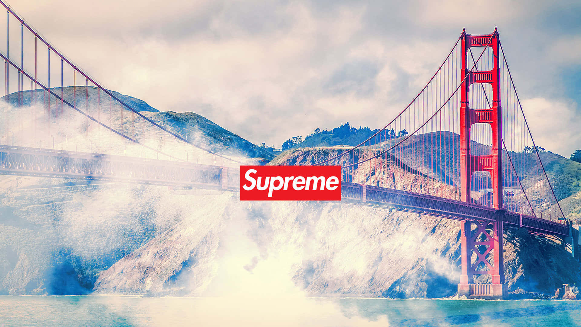 supreme 桌布 壁紙 — 金門大橋在霧氣瀰漫的山丘前傲然聳立，水面上疊加了一個紅色的Supreme標誌。