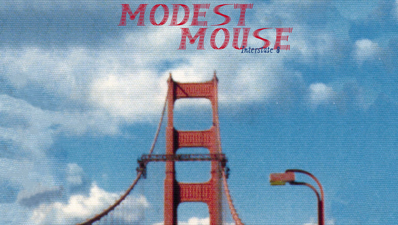 Modest 桌布 壁紙 — 金門大橋塔樓在明亮的藍天下，有蓬鬆的白雲和紅色文字寫著 Modest Mouse。