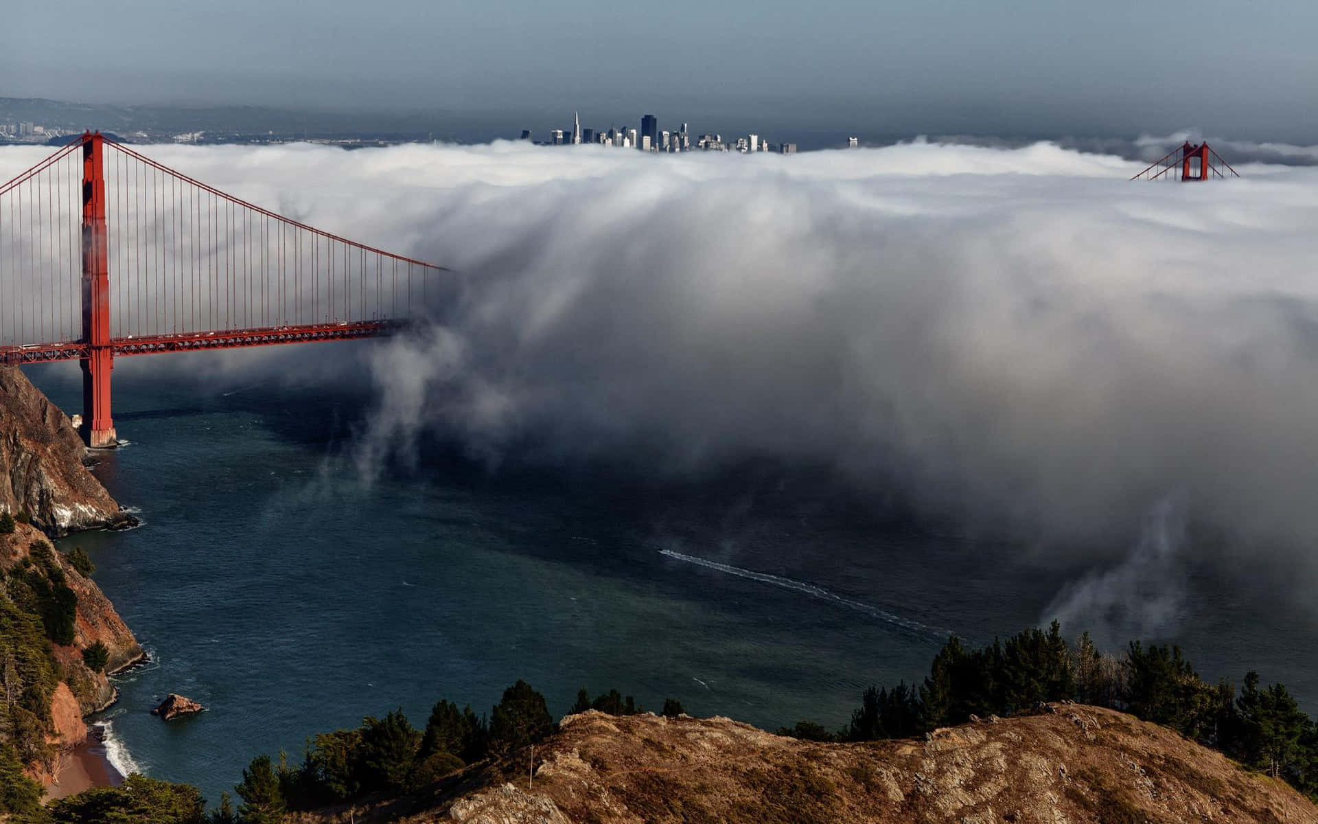 San Francisco 桌布 壁紙 — 金門大橋從濃厚的霧海中浮現，上方可見舊金山的天際線，一艘船在下方水面滑行。