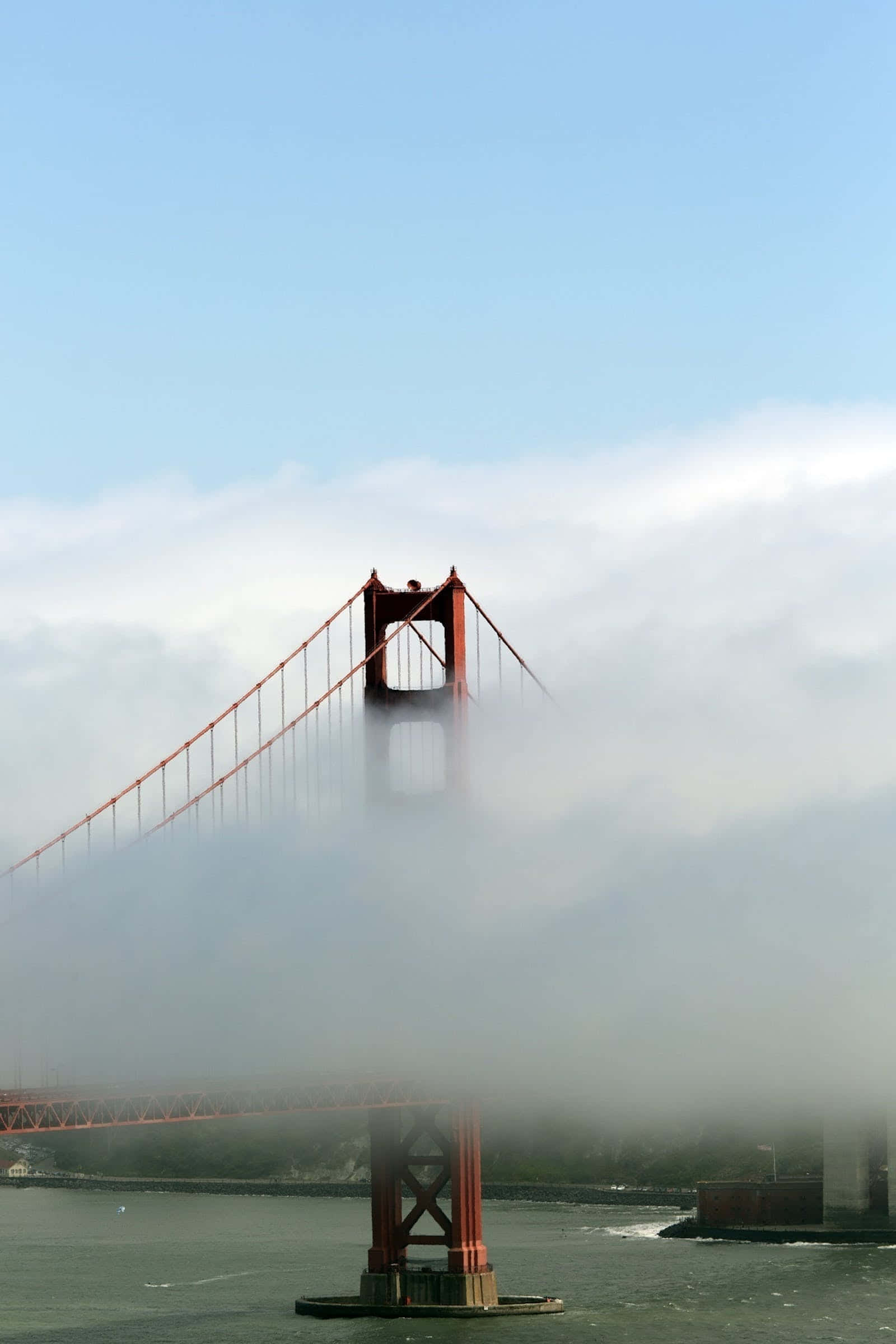 California Aesthetic 桌布 壁紙 — 金門大橋從濃霧中浮現，其標誌性的橙色橋塔刺穿平靜水面上方的淡藍色天空。