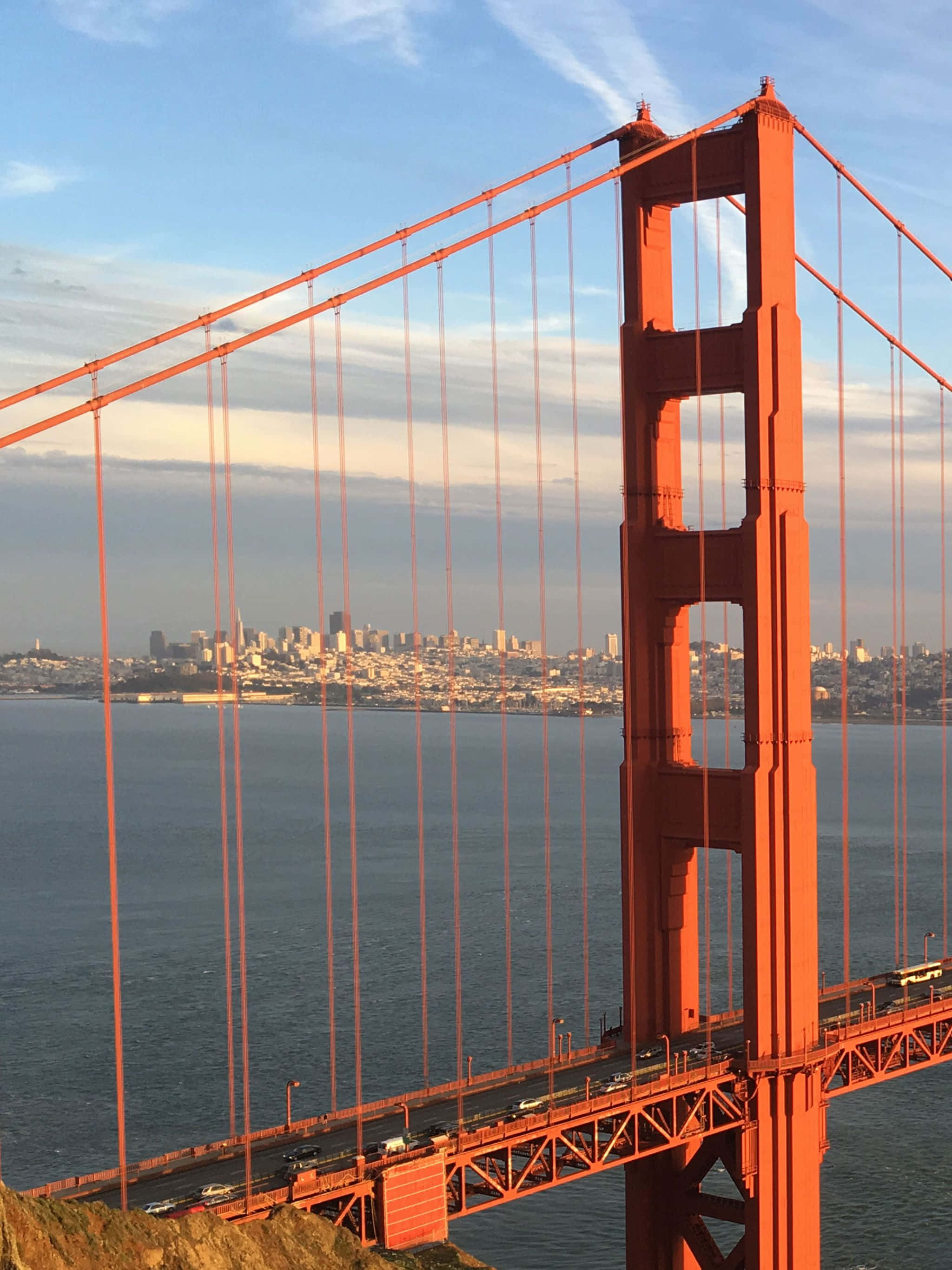 bridge 桌布 壁紙 — 金門大橋的橋塔以鮮豔的橙色，襯托柔和的藍天、城市天際線和下方的水面。