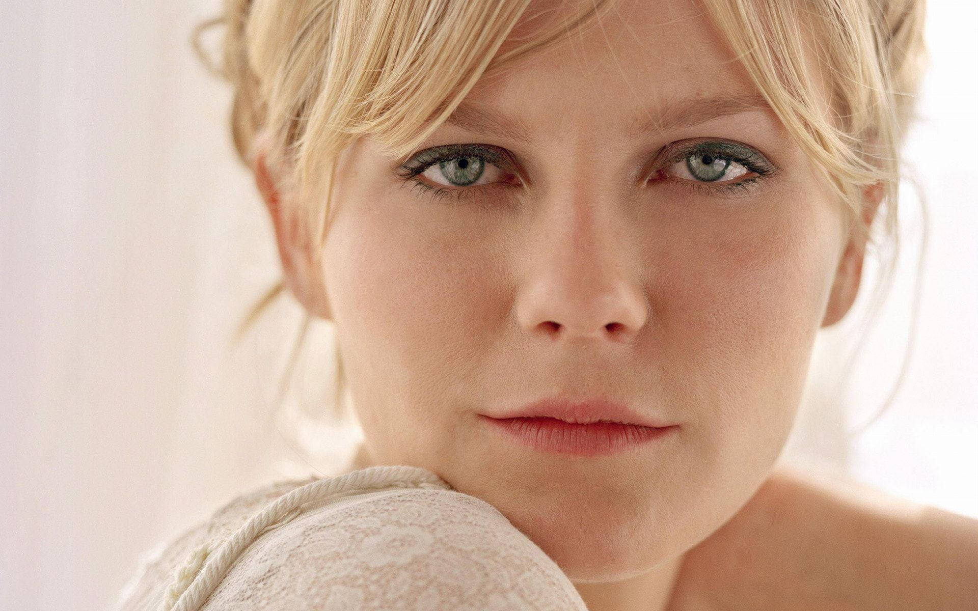 Kirsten Dunst 桌布 壁紙 — 金髮女子特寫肖像，擁有引人注目的綠色眼睛，直視觀眾，背景為柔和的白色。