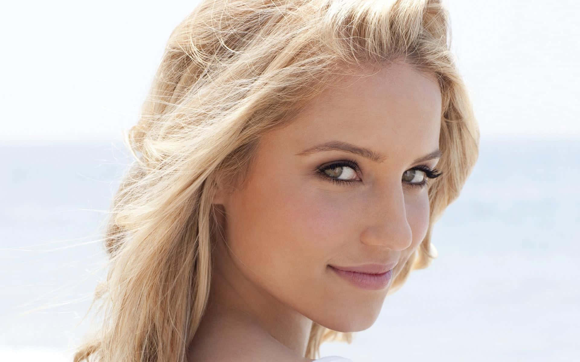 dianna agron 桌布 壁紙 — 金髮女子的特寫肖像，帶著溫柔的微笑，背景是明亮模糊的海洋。