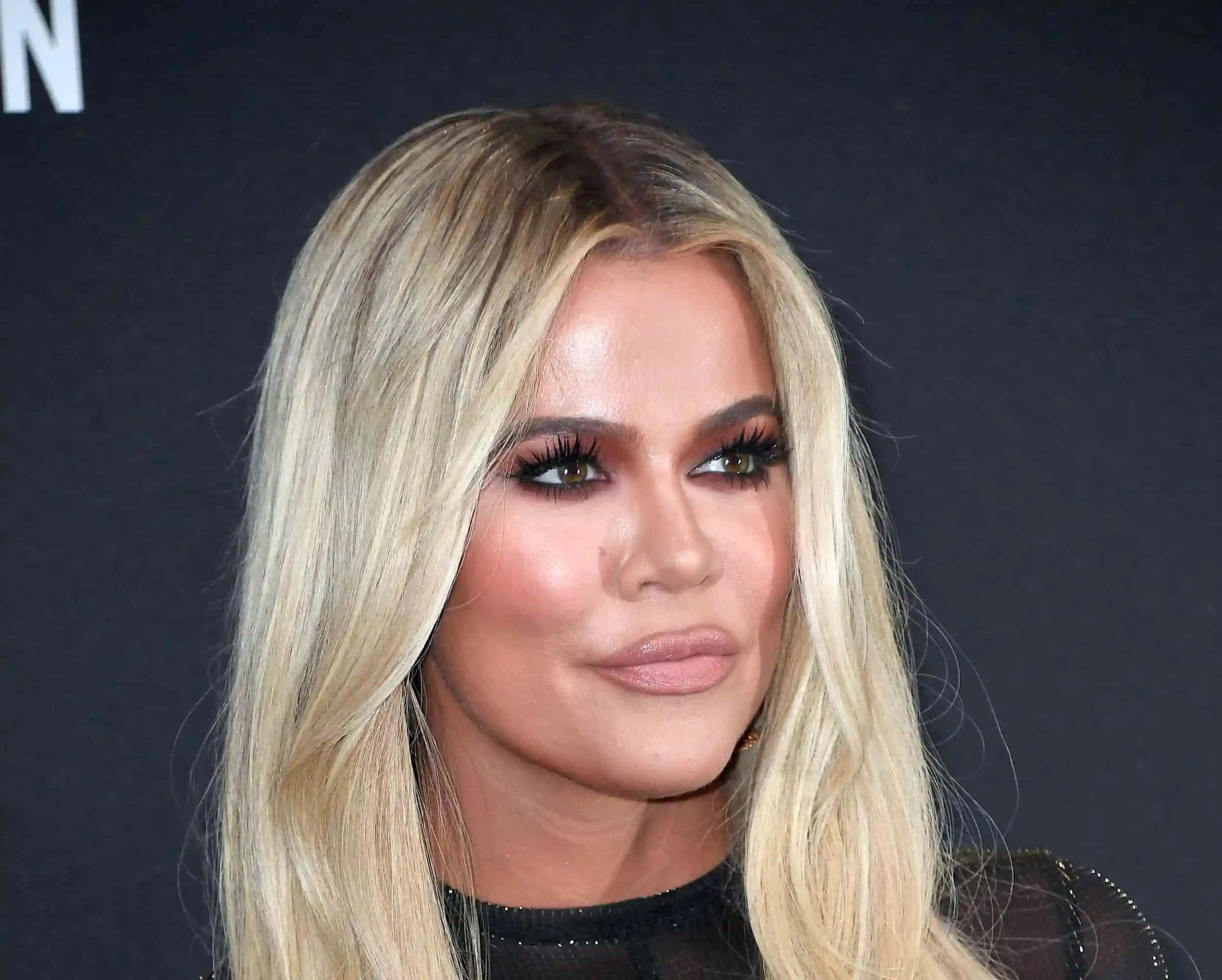 Khloe Kardashian 桌布 壁紙 — 金髮女性的特寫肖像，擁有戲劇性的睫毛和柔和化妝，背景是深色。