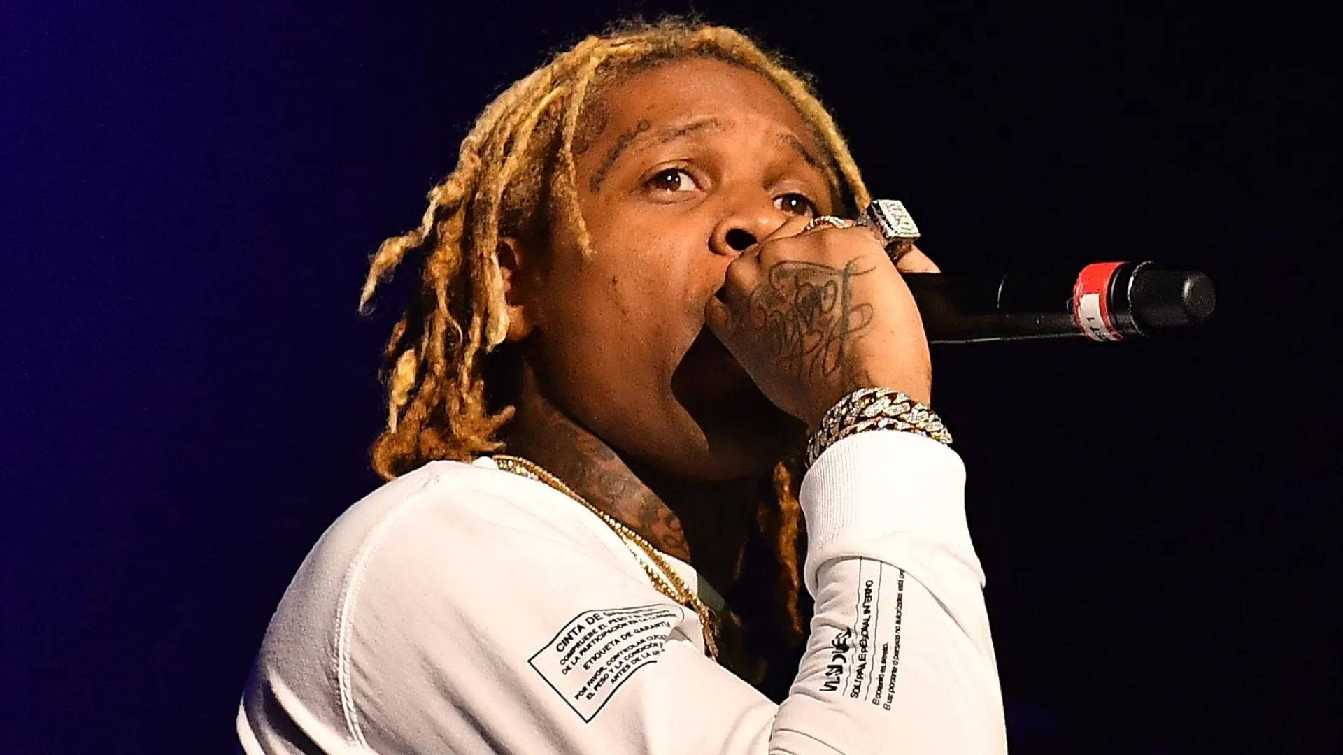 Lil Durk 桌布 壁紙 — 金髮辮子說唱歌手在藍色舞台燈光下，穿著白襯衫和戴金鏈，對著麥克風唱歌。