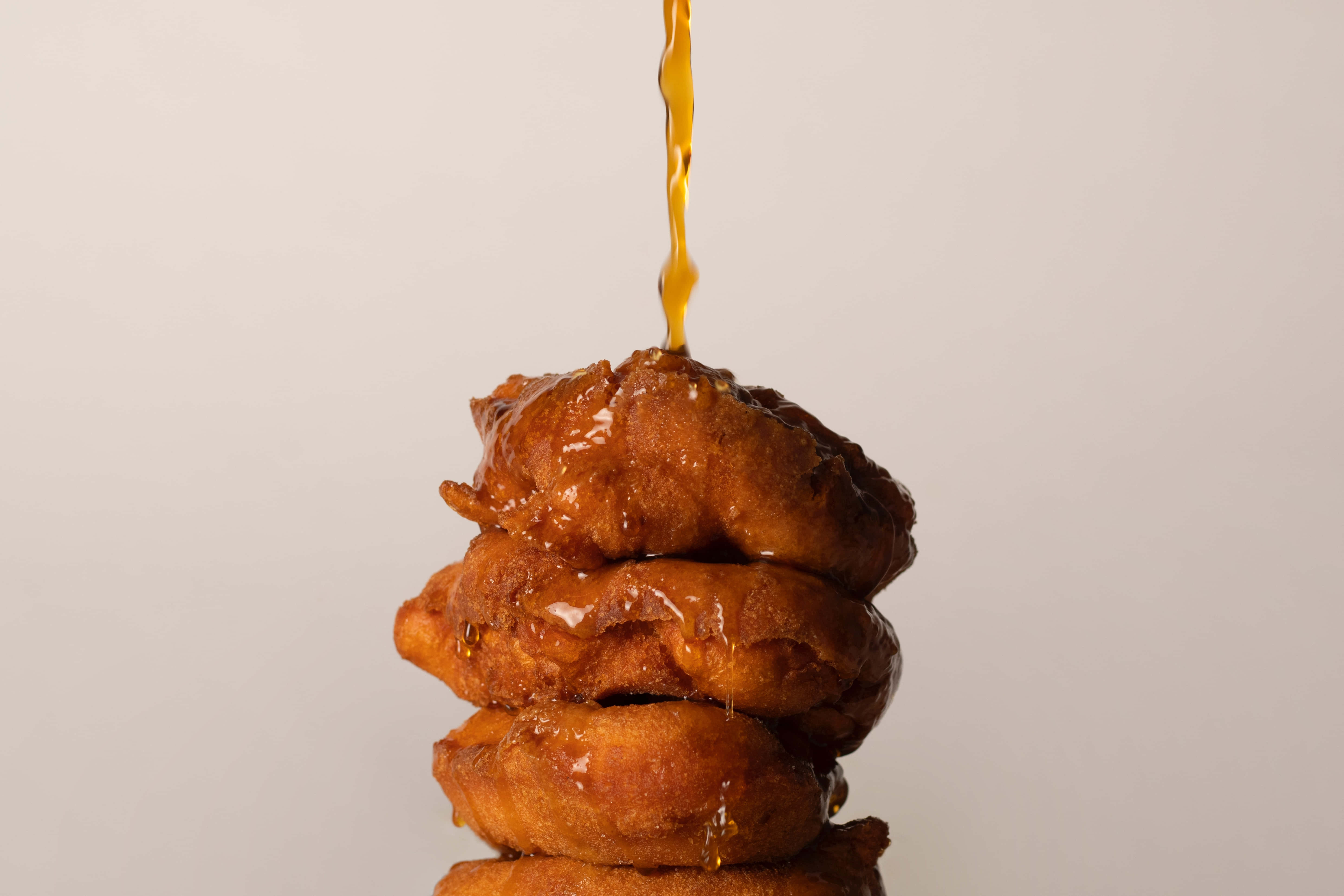 Caramel 桌布 壁紙 — 金黃糖漿如瀑布般流下，澆在酥脆炸甜甜圈塔上，背景為中性色調。