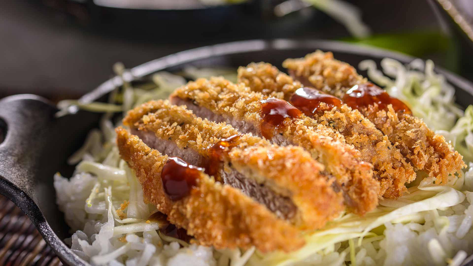 Food Photography 桌布 壁紙 — 金黃色切好的炸豬排，帶有光澤的醬汁，放在黑色鑄鐵鍋中的高麗菜絲上。