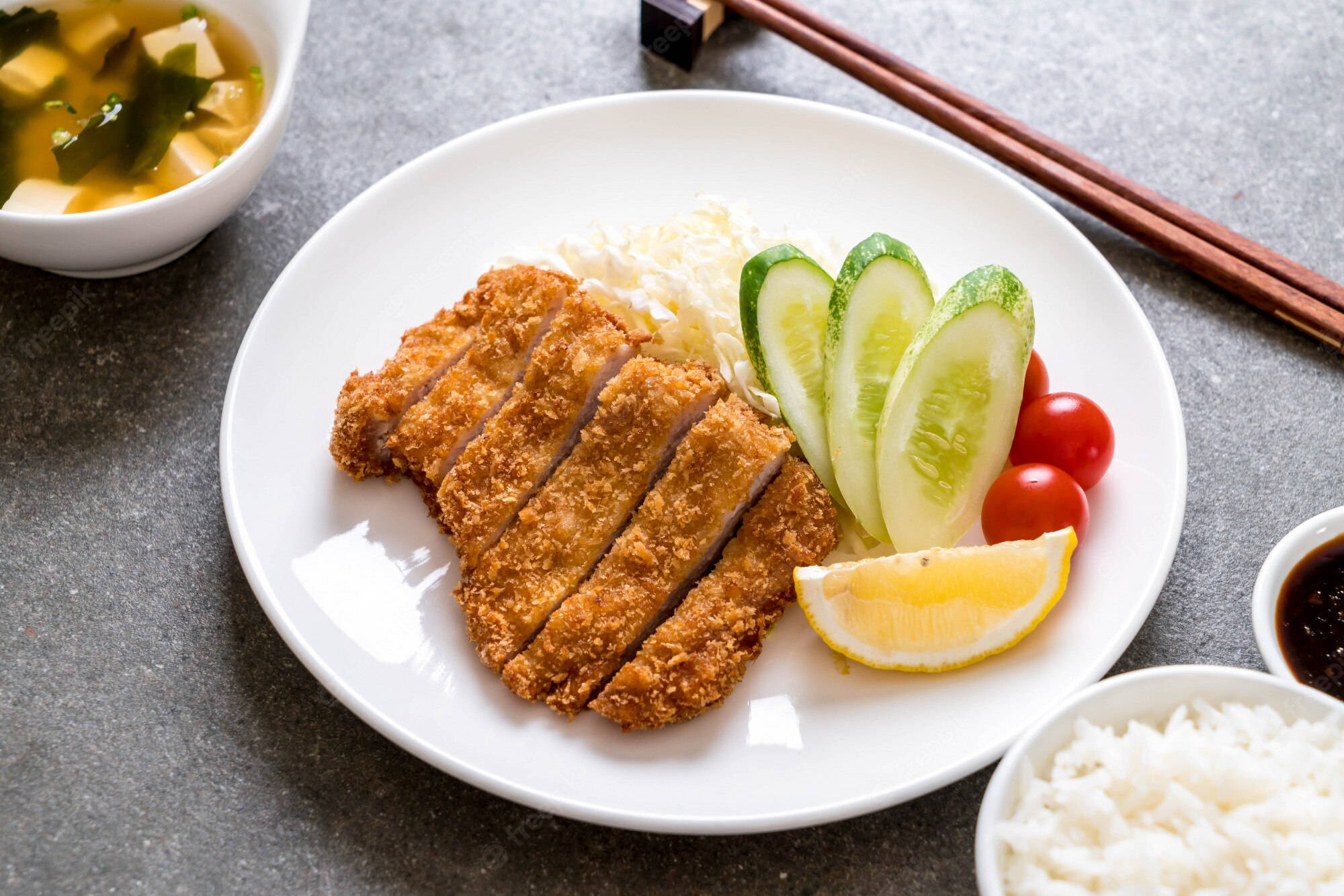 Food Photography 桌布 壁紙 — 金黃色切好的炸豬排，配上米飯、小黃瓜、番茄、檸檬和味噌湯，放在灰色桌上。