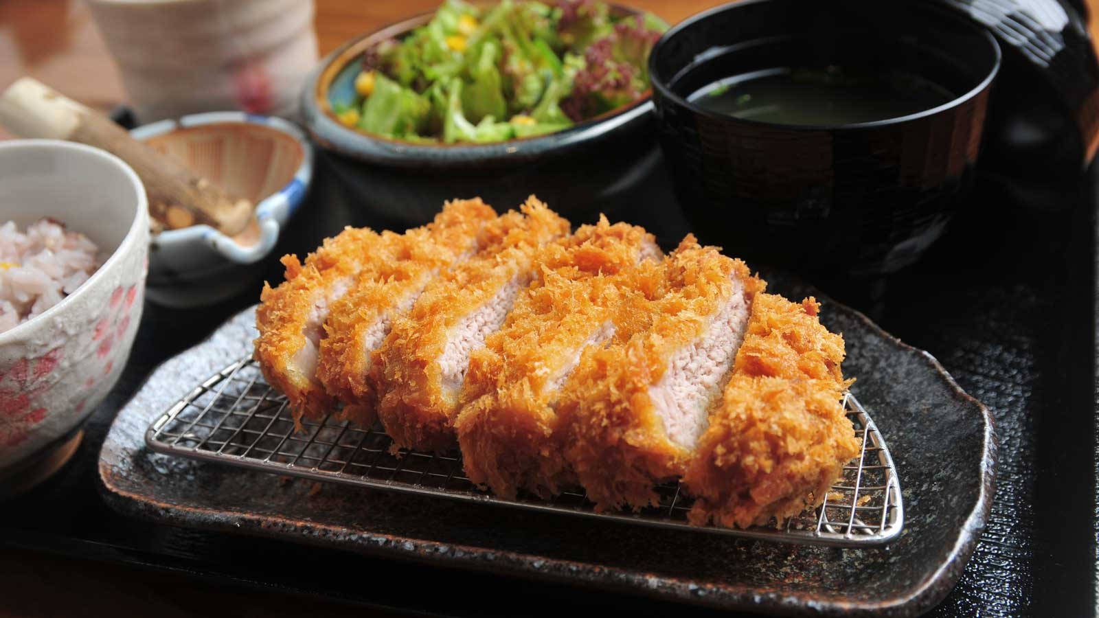 Food Photography 桌布 壁紙 — 金黃色切片炸豬排放在金屬架上，搭配米飯沙拉和味噌湯，盛裝在傳統日本碗中。