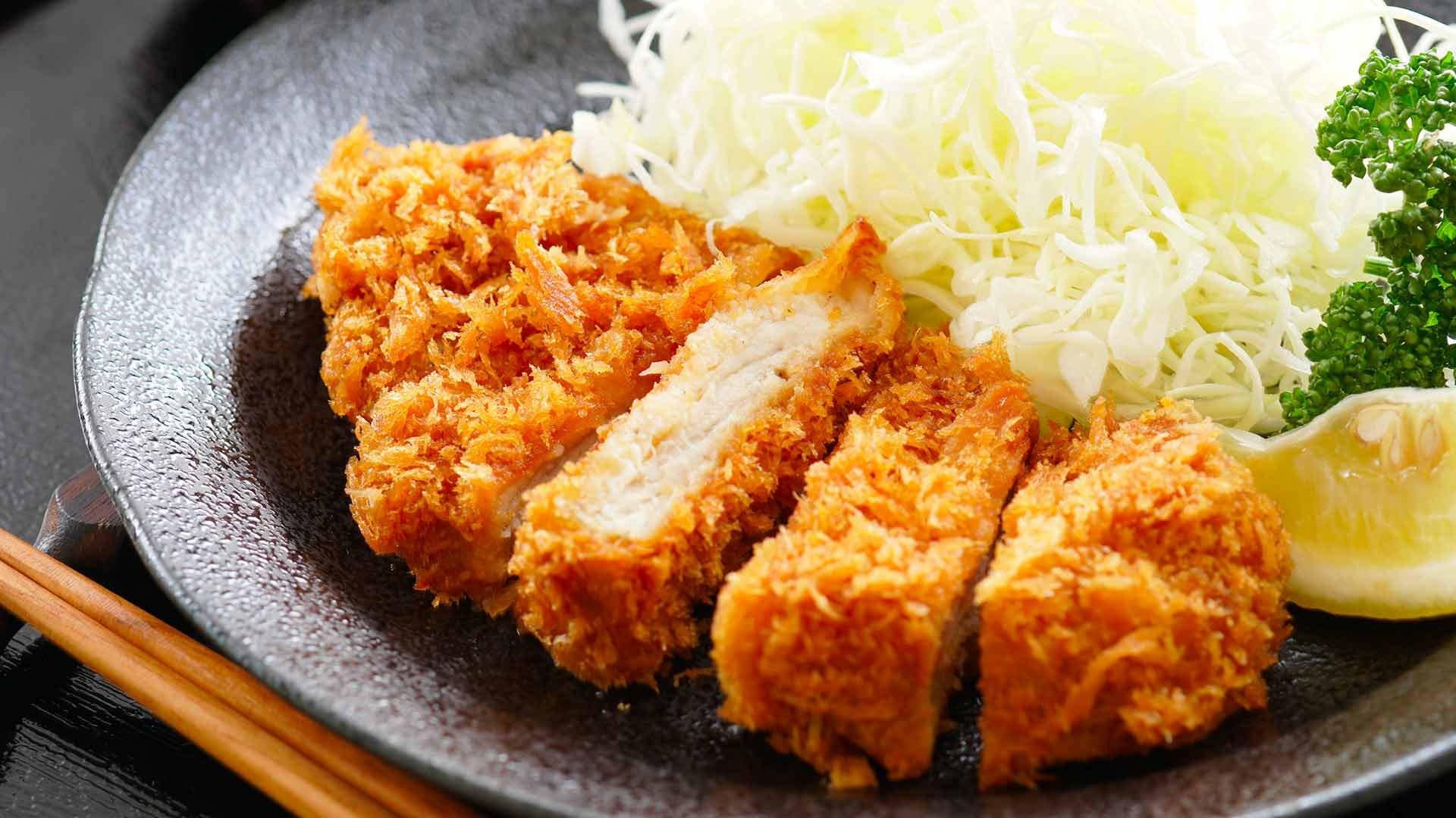 Food Photography 桌布 壁紙 — 金黃色切片炸豬排配高麗菜絲及檸檬角，置於深色紋理盤上。