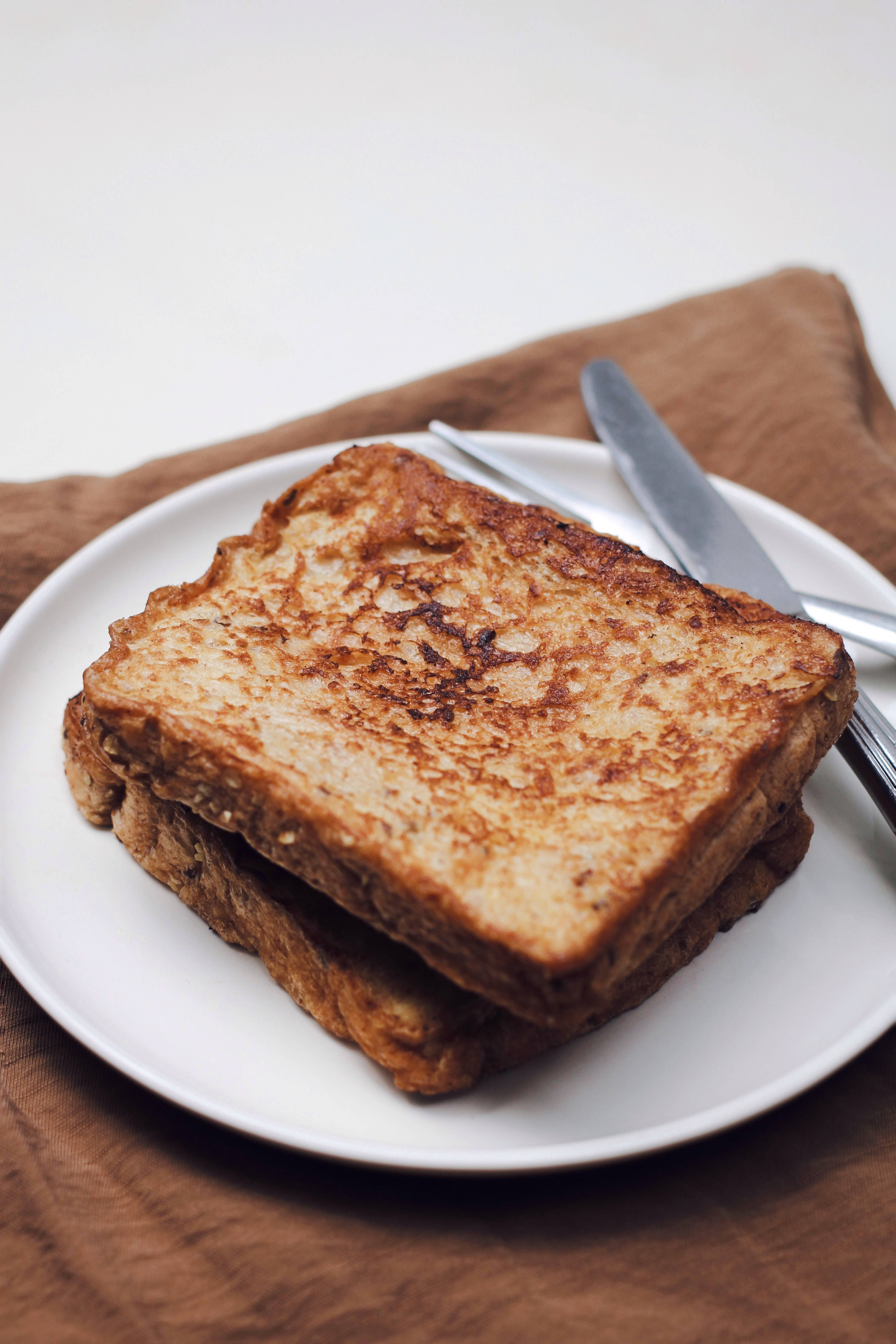 French Toast 桌布 壁紙 — 金黃色法式吐司堆疊在白色盤子上，旁邊有刀，置於棕色布上。