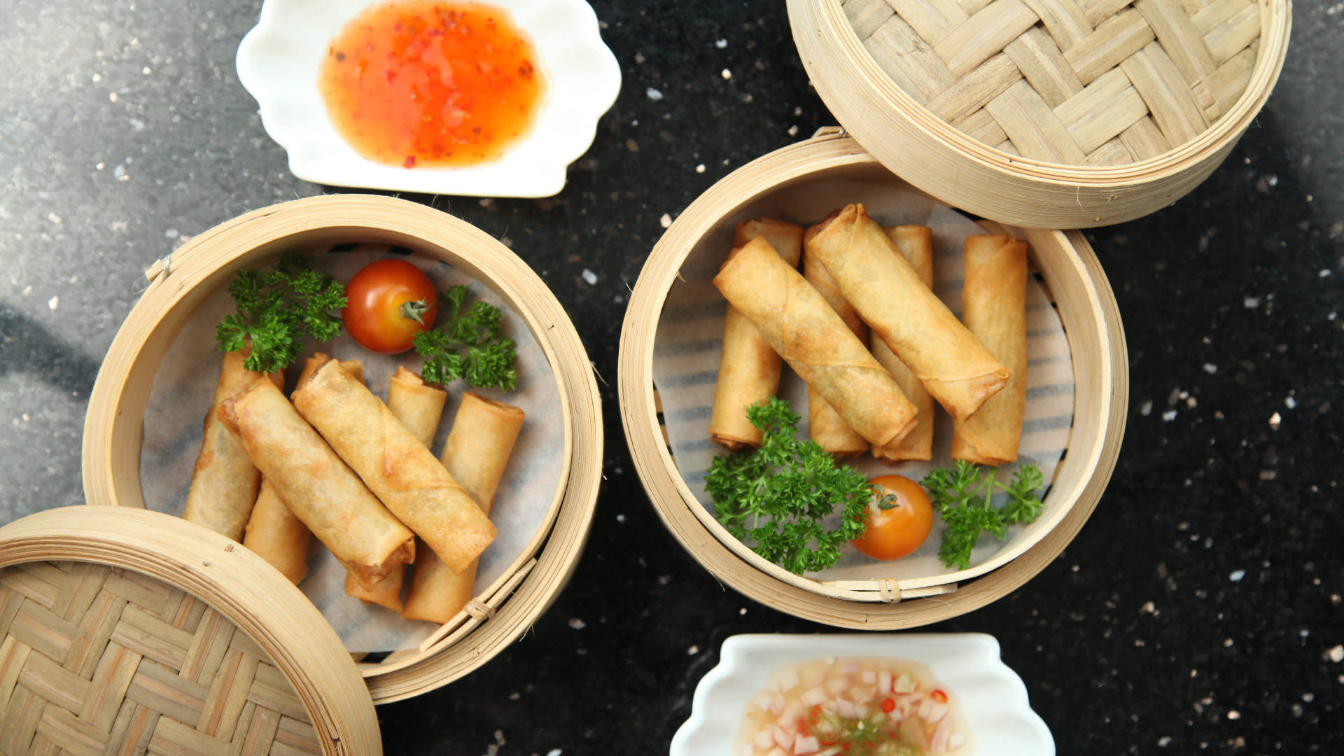 Egg 桌布 壁紙 — 金黃色炸春捲放在竹蒸籠裡，配上新鮮歐芹、小番茄和蘸醬，置於深色斑點表面上。