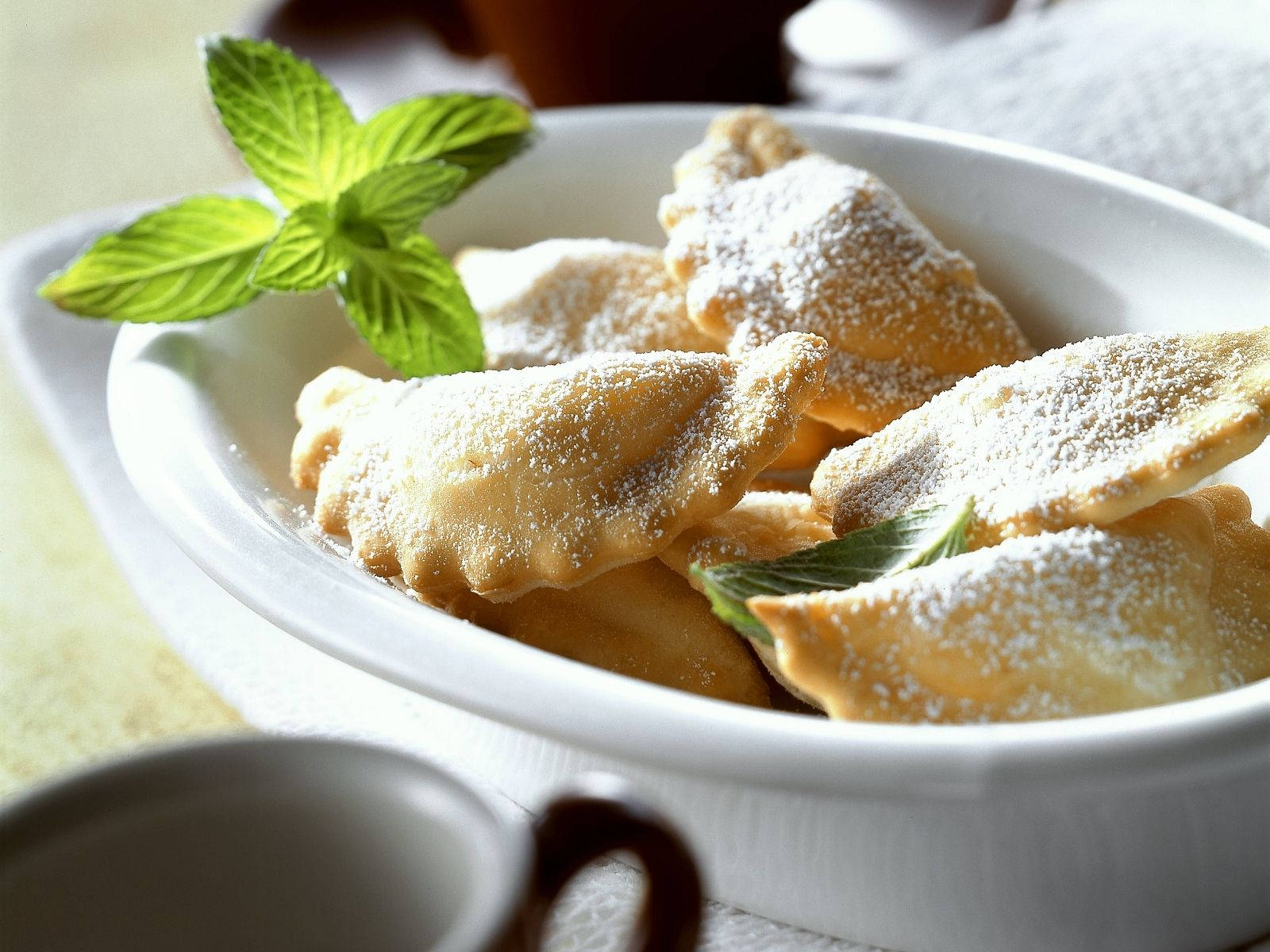 Food Photography 桌布 壁紙 — 金黃色炸糕點，撒上糖粉，並用新鮮薄荷葉點綴，放在白色陶瓷碗中。