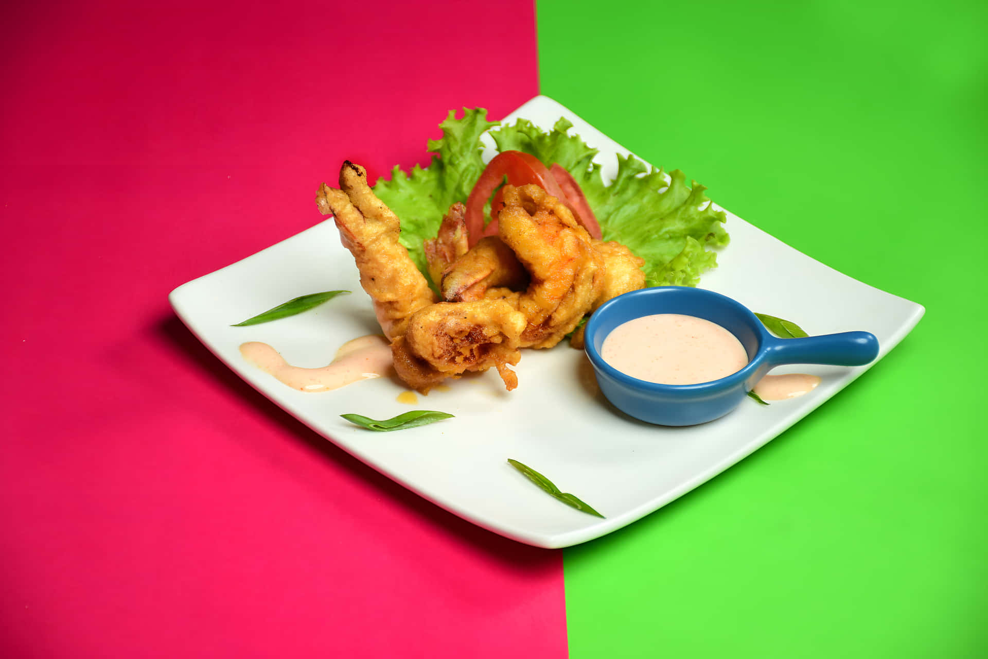 Fried prawn on a plate with white sauce 壁紙 — 金黃色炸蝦配生菜、番茄和蘸醬，放在白色盤子上，背景為粉紅和綠色分割。