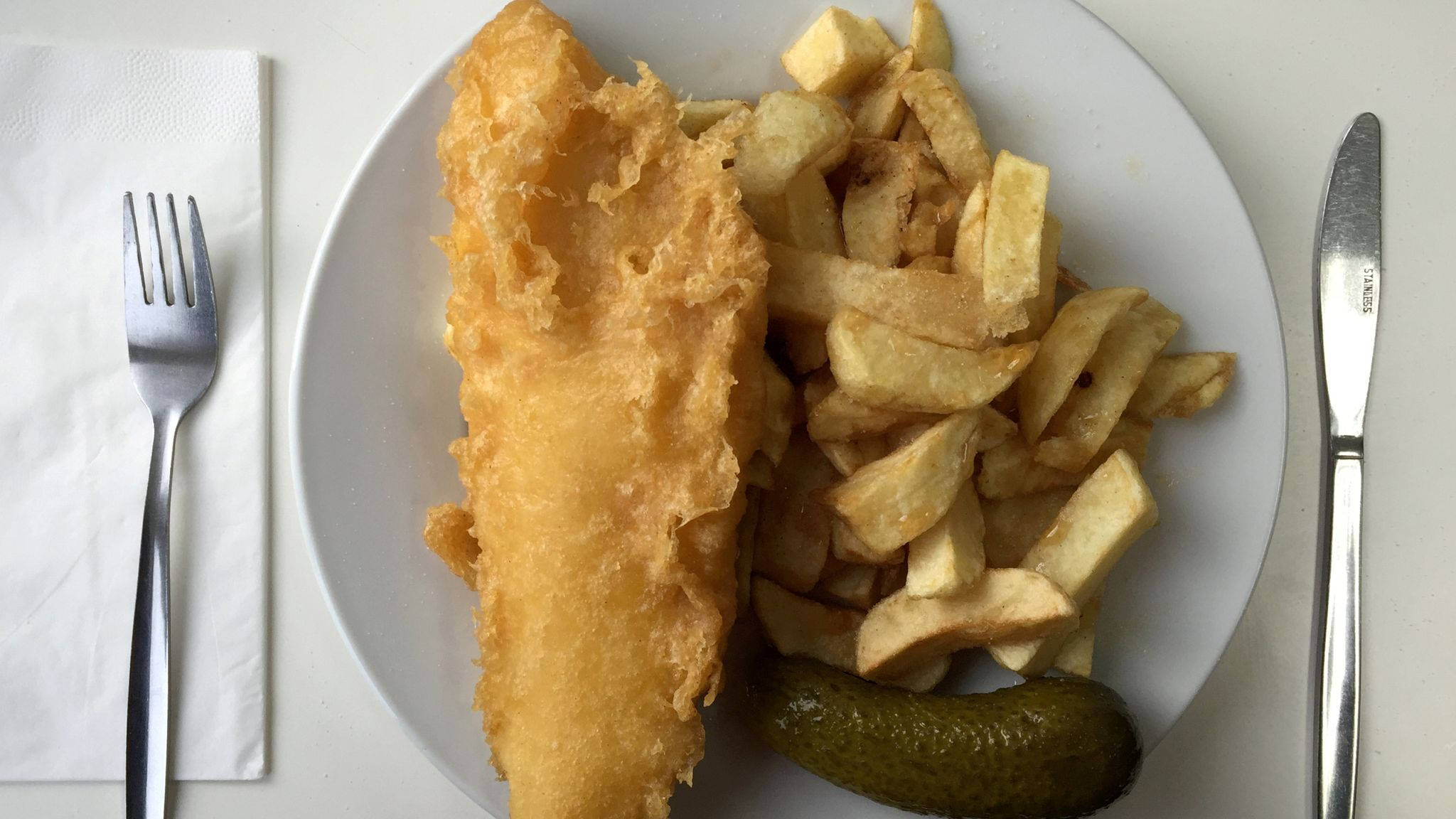 Pickle 桌布 壁紙 — 金黃色炸魚和厚切薯條，盛裝在白色盤子上，搭配酸黃瓜條和餐具。