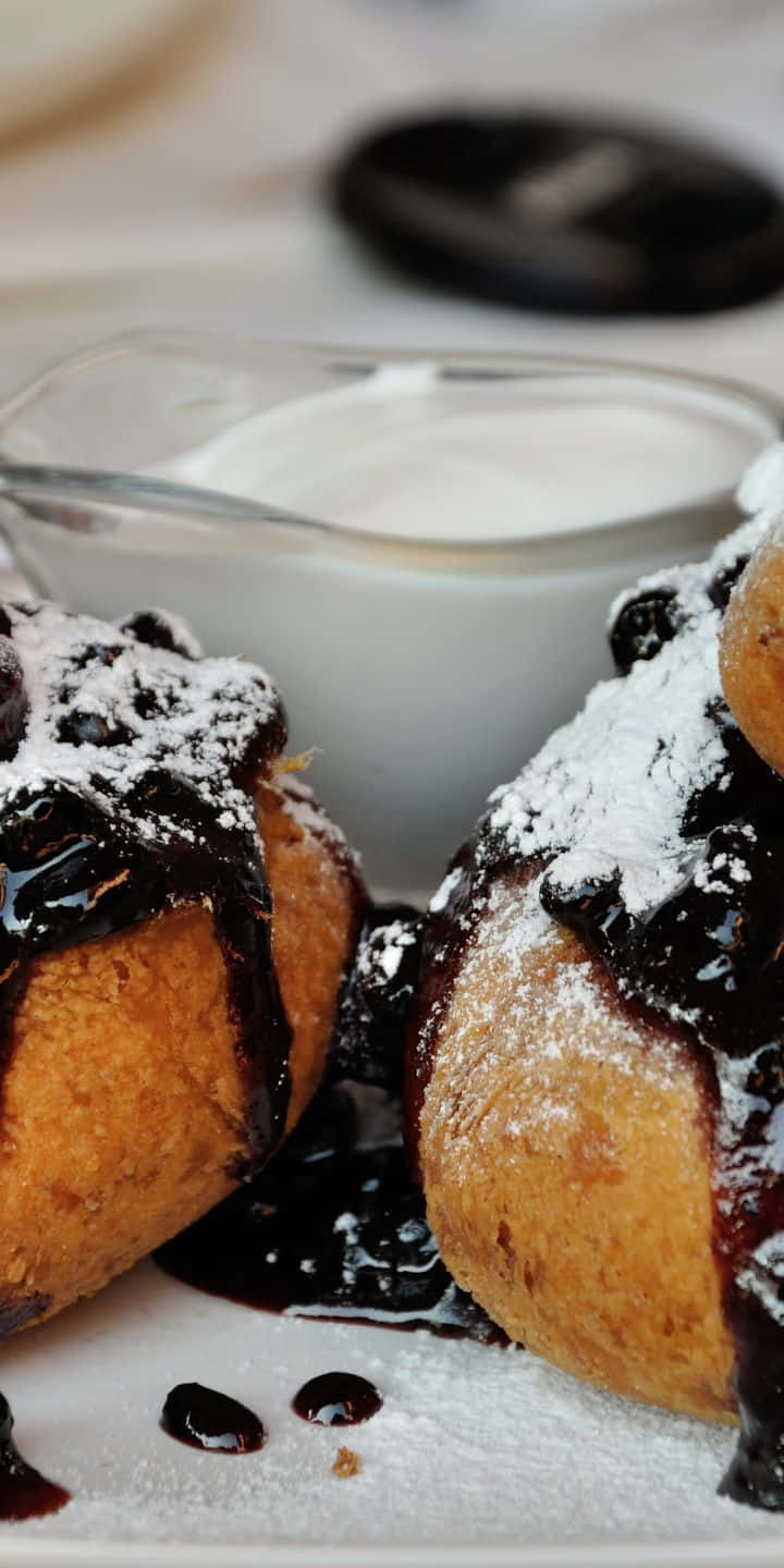 Pastry 桌布 壁紙 — 金黃色炸麵團糕點，淋上深色糖漿，撒上糖粉，旁邊放著一小碗奶油。