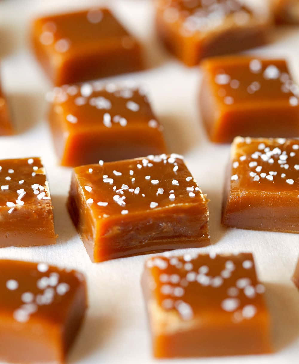 Brown Caramel 桌布 壁紙 — 金黃色焦糖方塊上撒有粗鹽，放在白色烘焙紙上，景深較淺。