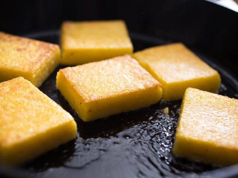 Food Photography 桌布 壁紙 — 金黃色玉米糕塊在黑色煎鍋的深色油中滋滋作響，蒸汽升騰。