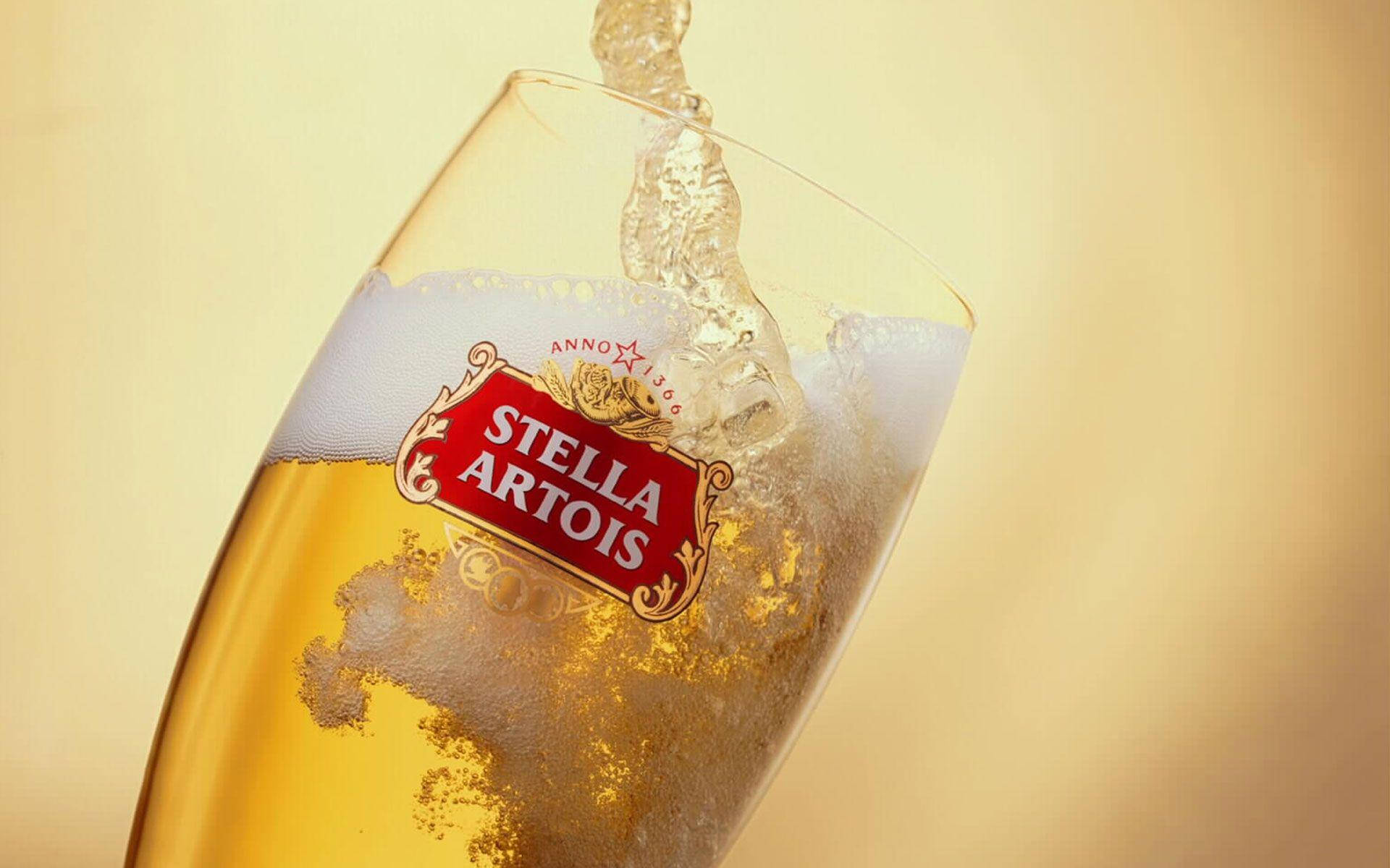 Drink 桌布 壁紙 — 金黃色的Stella Artois啤酒倒入玻璃杯中，在溫暖的米色背景上形成泡沫豐富的頂層。