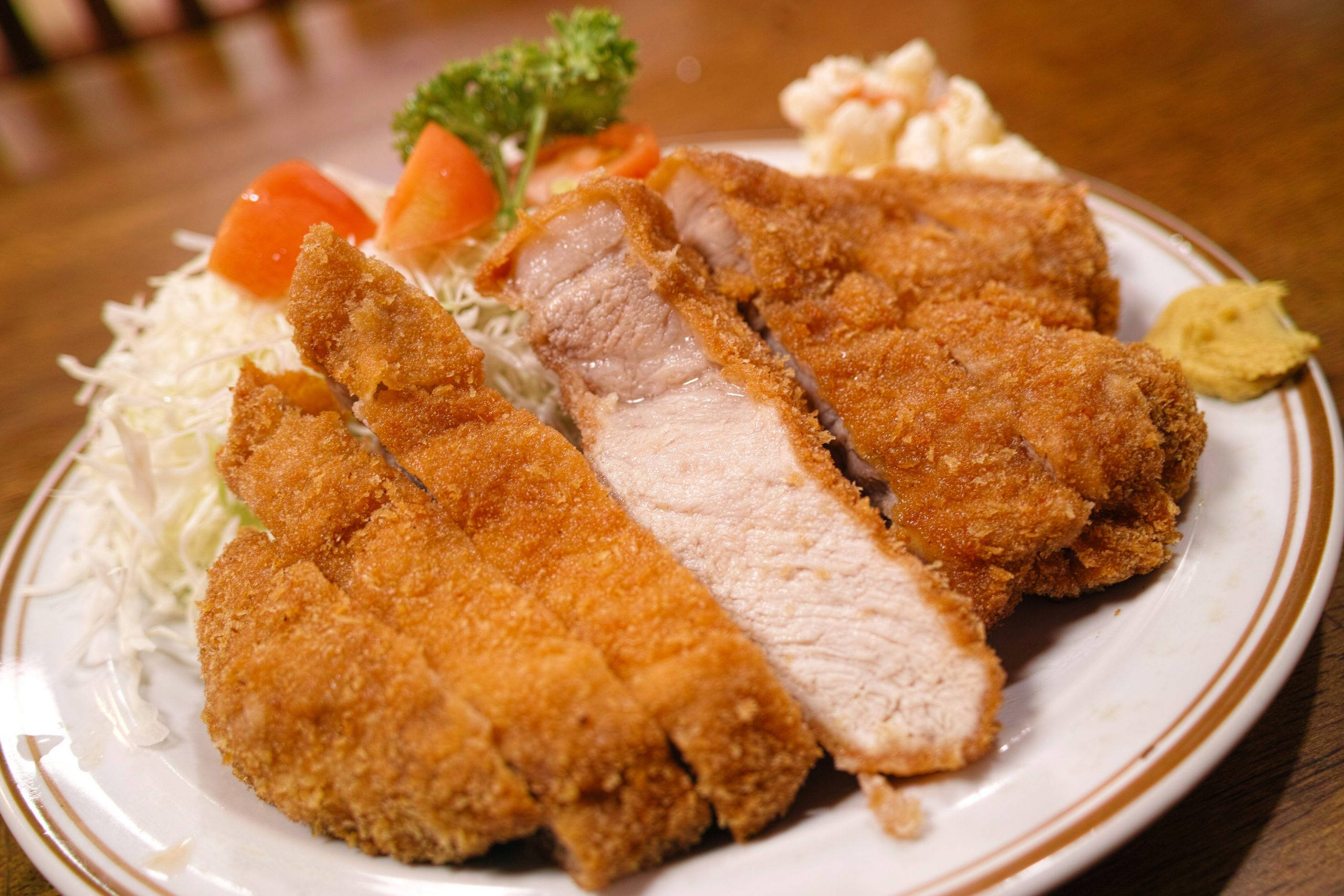 Food Photography 桌布 壁紙 — 金黃色的切片炸豬排，外皮酥脆，放在高麗菜絲、番茄和配菜上，置於木桌上。