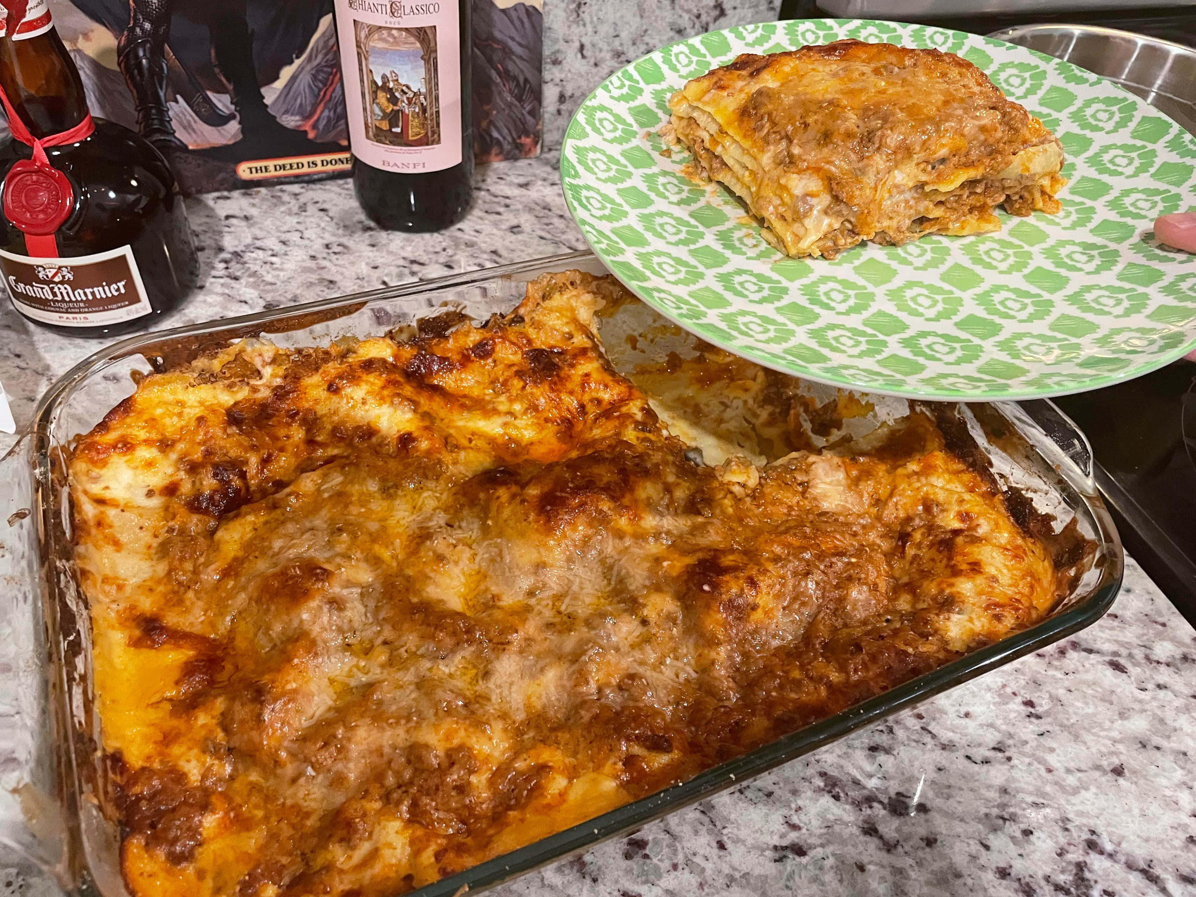 Pasta 桌布 壁紙 — 金黃色的千層麵配上融化的起司，盛在綠色圖案盤上，從玻璃烤盤中取出，放在有斑點的檯面上。