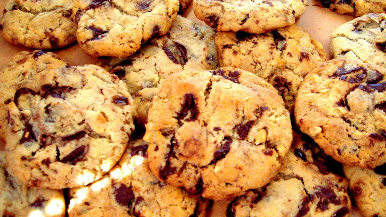 720p Cookies 桌布 壁紙 — 金黃色的巧克力曲奇高高堆起，帶有融化的巧克力塊和溫暖的烘焙質感。