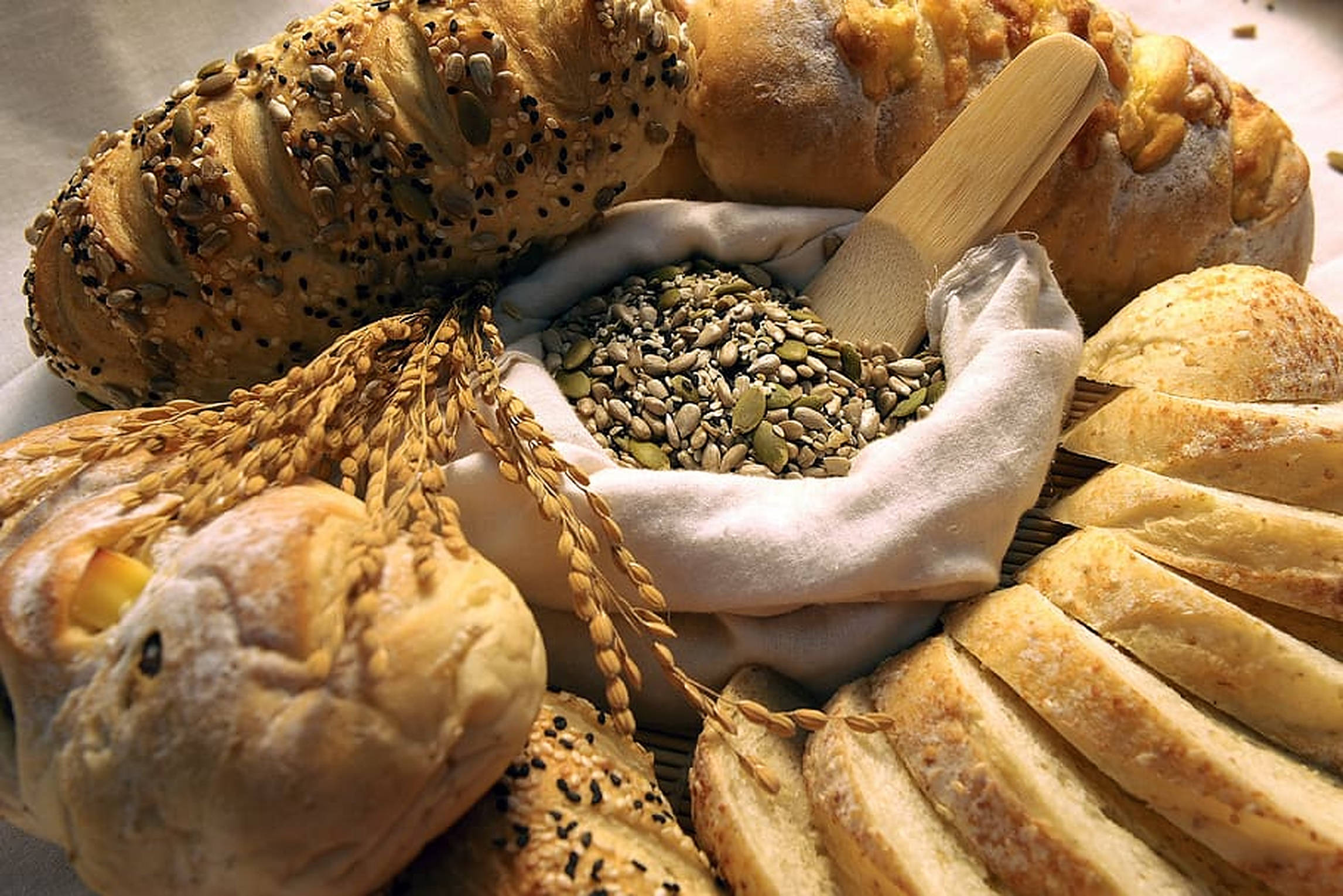 Bakery 桌布 壁紙 — 金黃色的手工麵包和葵花籽放在一個布袋裡，還有麥稈。