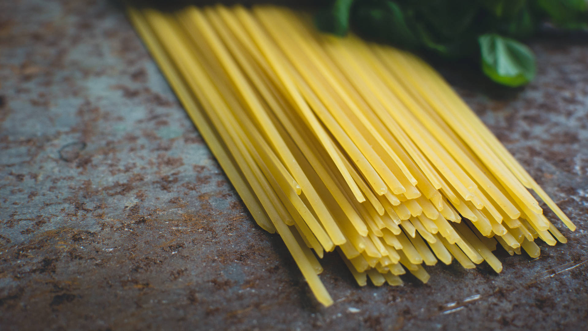 Pasta 桌布 壁紙 — 金黃色的未煮熟義大利麵條放在經風化的鏽蝕金屬表面上，附近有新鮮的羅勒葉。