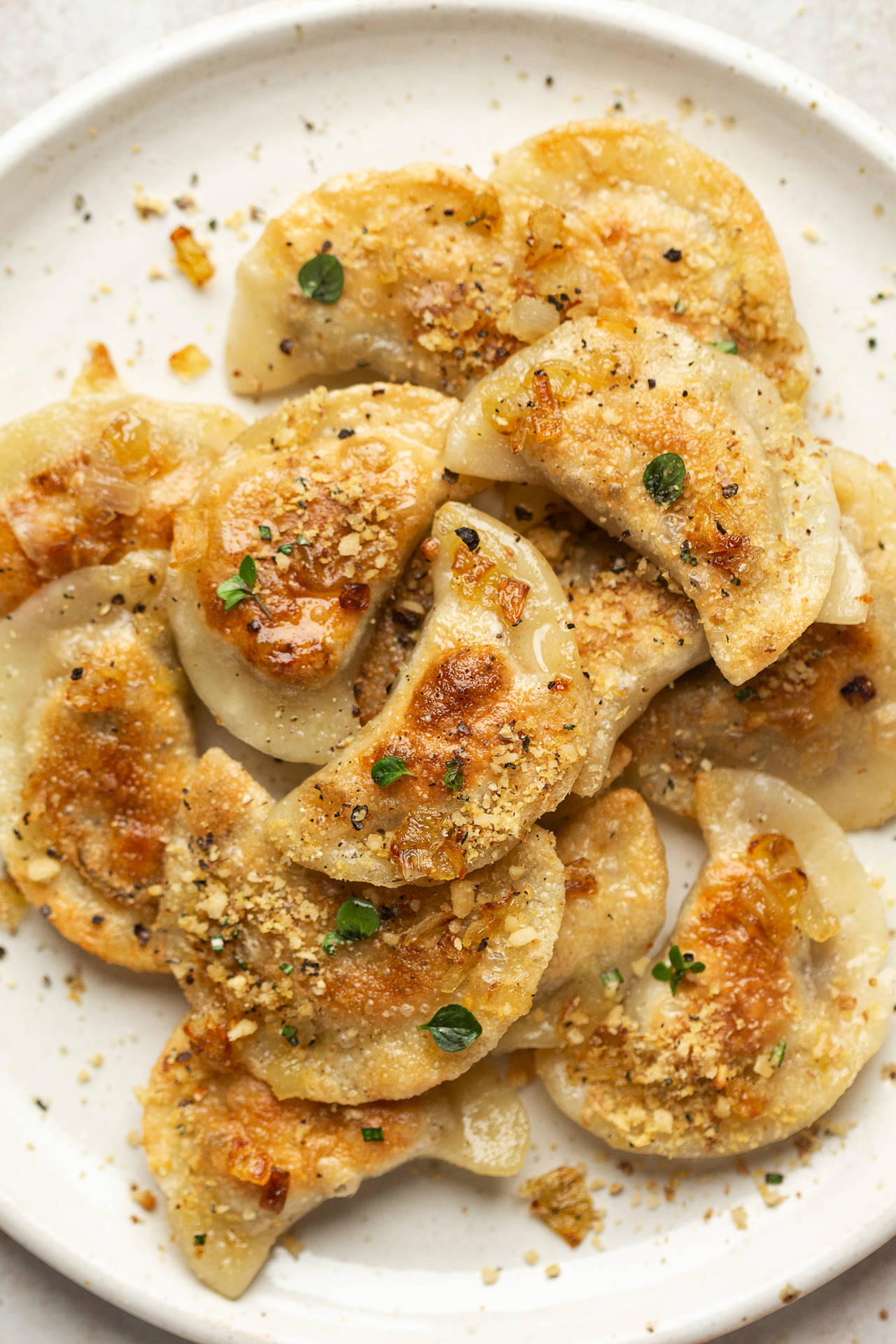 Food Photography 桌布 壁紙 — 金黃色的波蘭餃子上面撒上酥脆的蒜蓉麵包糠和新鮮香草，堆放在白色圓點盤子上。