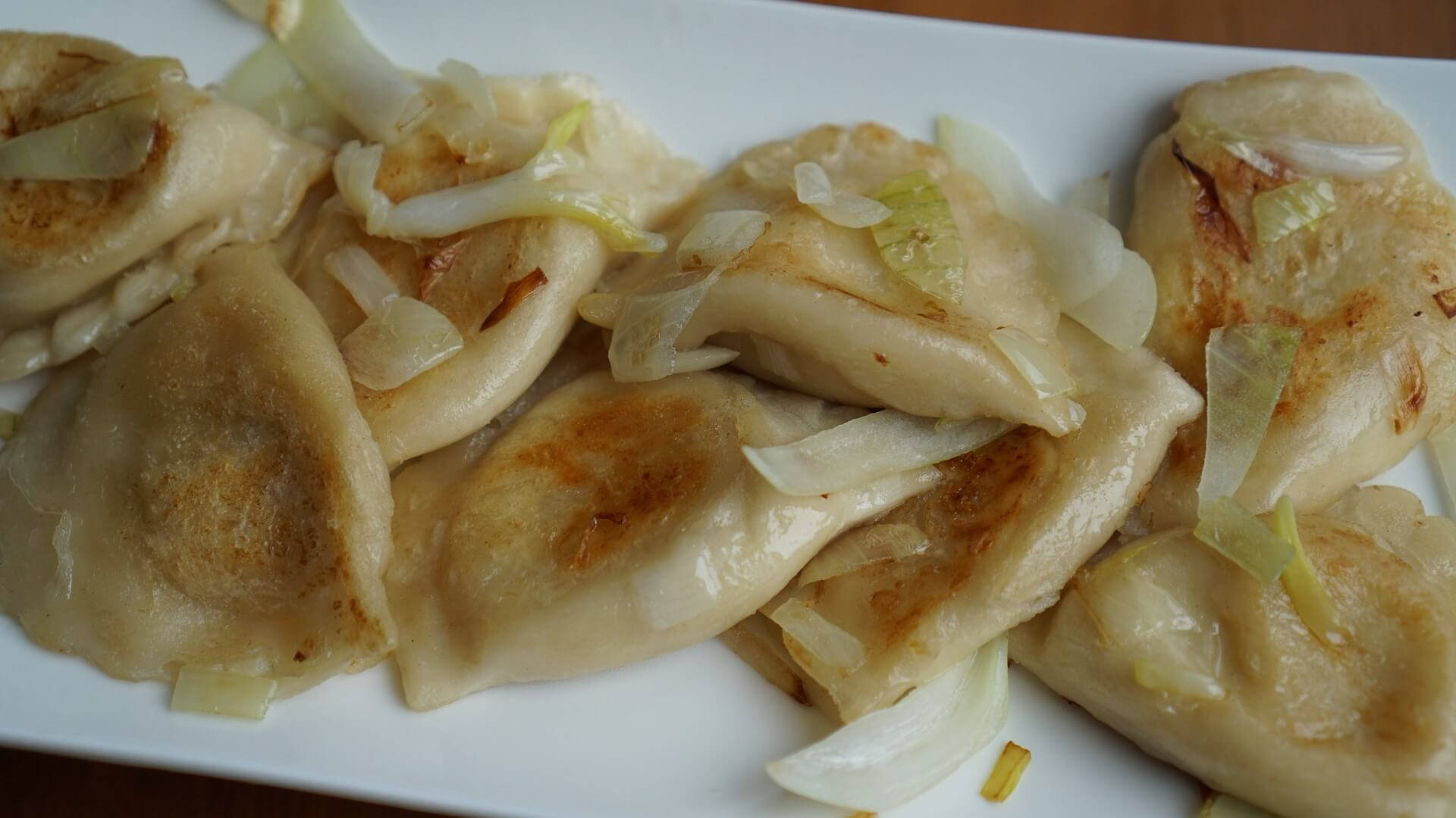 yummy 桌布 壁紙 — 金黃色的波蘭餃子配上焦糖洋蔥，在暖光下於白色盤子上閃閃發光。