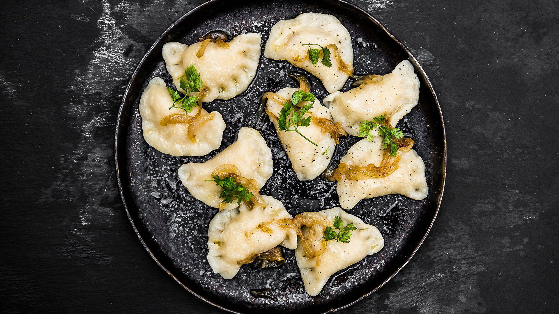 Food Photography 桌布 壁紙 — 金黃色的波蘭餃子配上焦糖洋蔥和新鮮歐芹，放在質樸的黑色盤子上，背景為深色紋理。