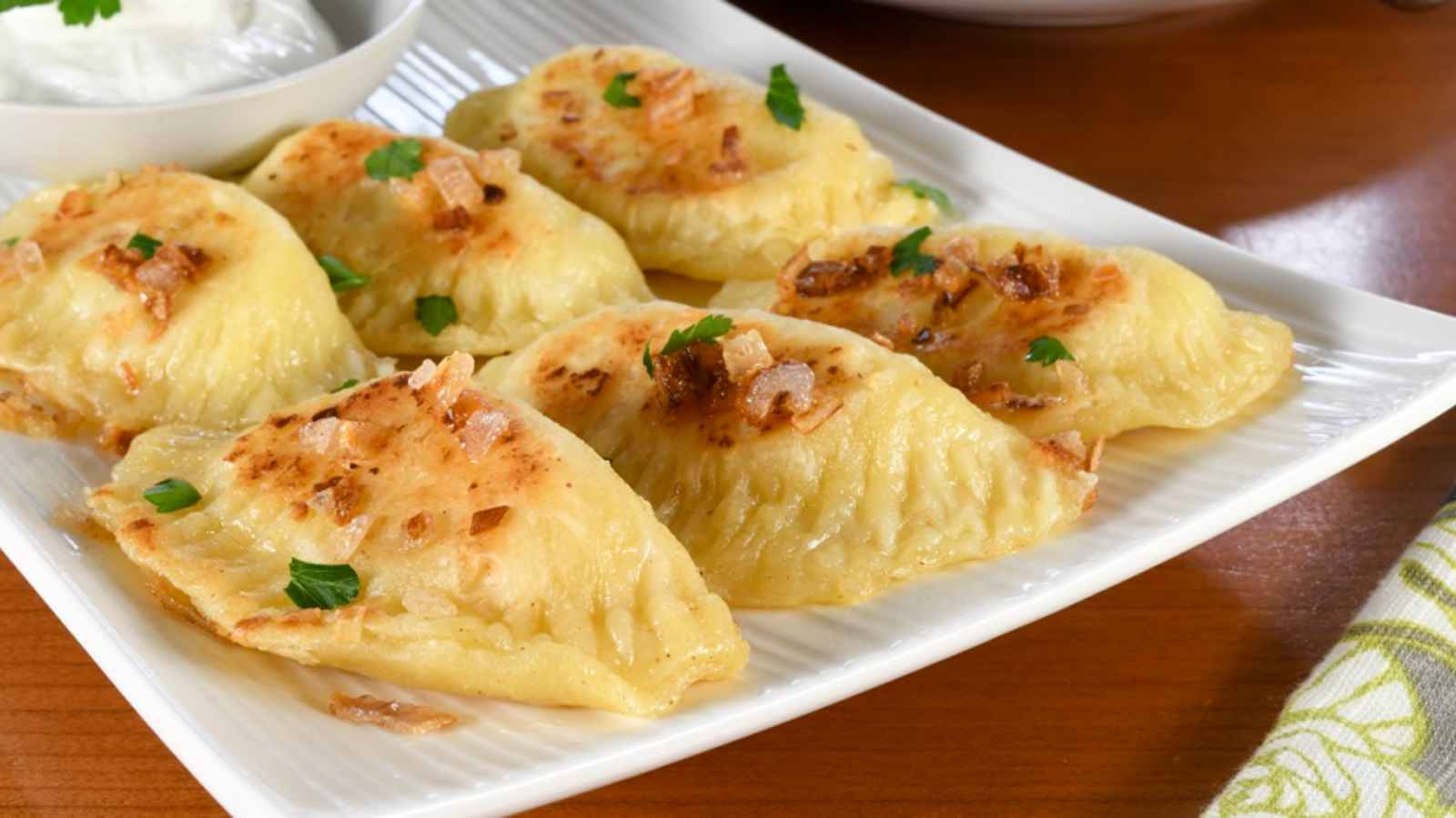 Food Photography 桌布 壁紙 — 金黃色的波蘭餃子配上酥脆洋蔥和新鮮歐芹，放在白色盤子上，令人食指大動。