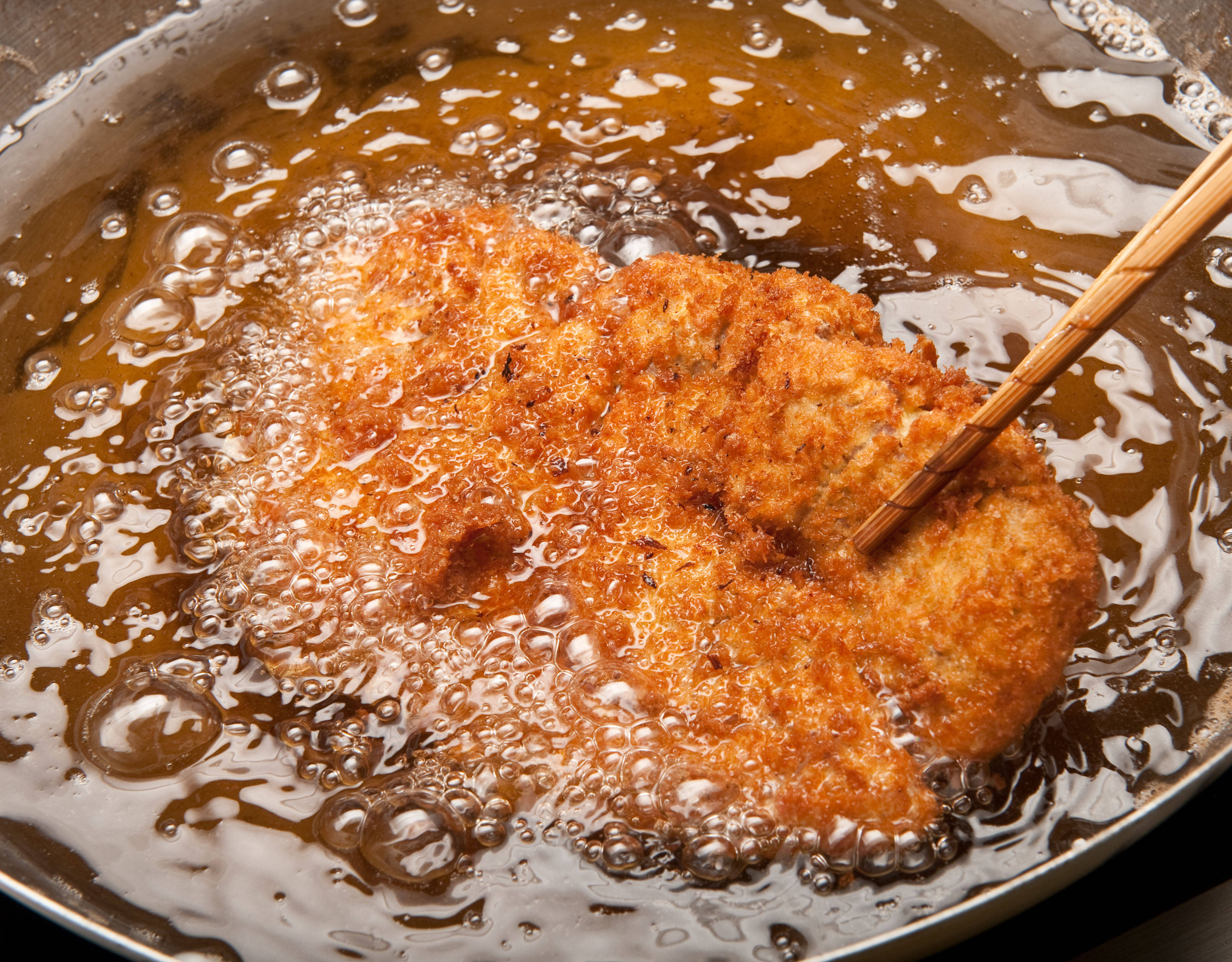 Food Photography 桌布 壁紙 — 金黃色的炸肉排在滾燙的油中滋滋作響，筷子將其從不鏽鋼鍋中夾起。