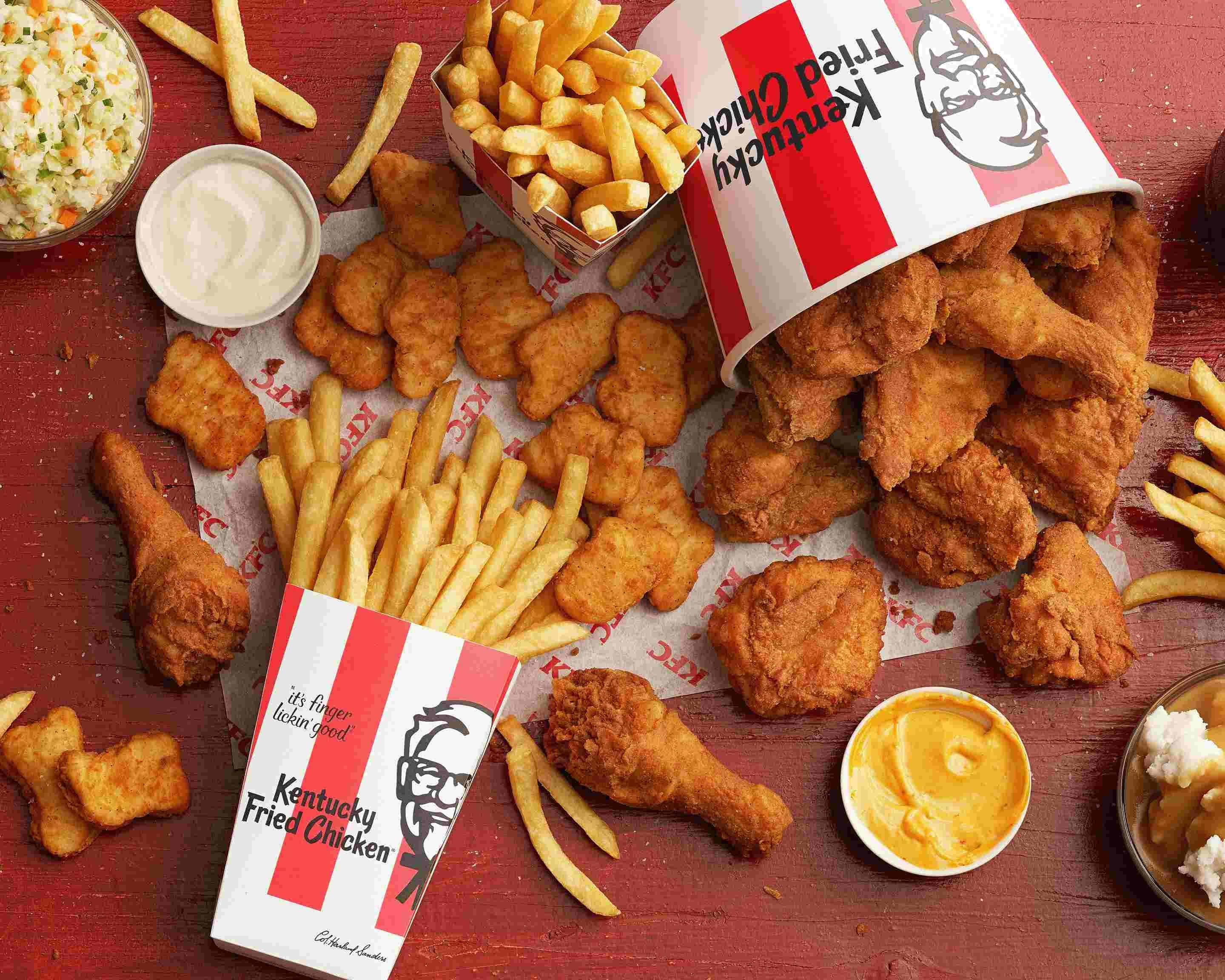 Kfc 桌布 壁紙 — 金黃色的炸雞塊和香脆薯條從品牌桶中溢出，放在質樸的紅色木桌上，附有蘸醬。