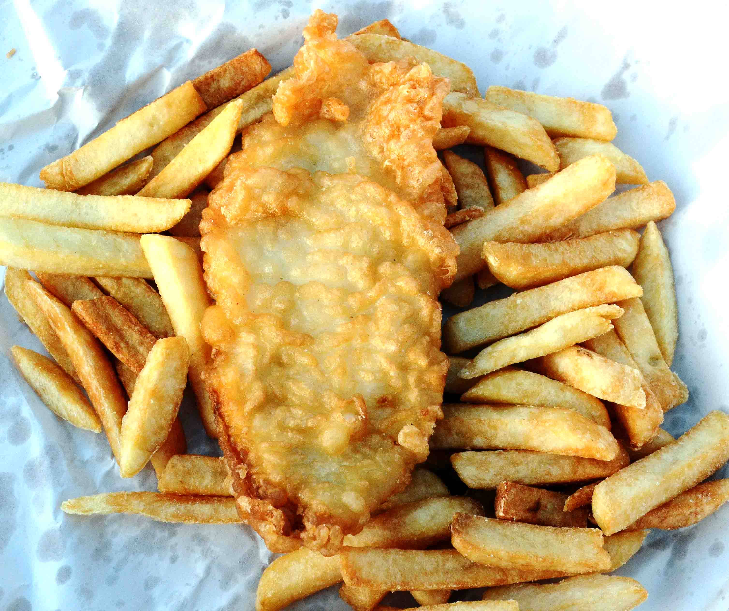 French Fries 桌布 壁紙 — 金黃色的炸魚薯條放在皺巴巴的紙上，酥脆的薯條圍繞著一塊裹粉的魚柳。