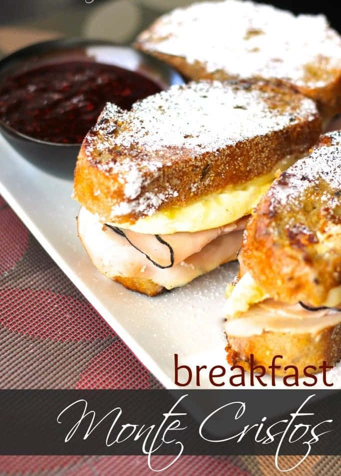 Black Forest Ham 桌布 壁紙 — 金黃色的烤蒙特克里斯托三明治撒上糖粉，放在盤子上，旁邊有一小碗深色莓果醬。