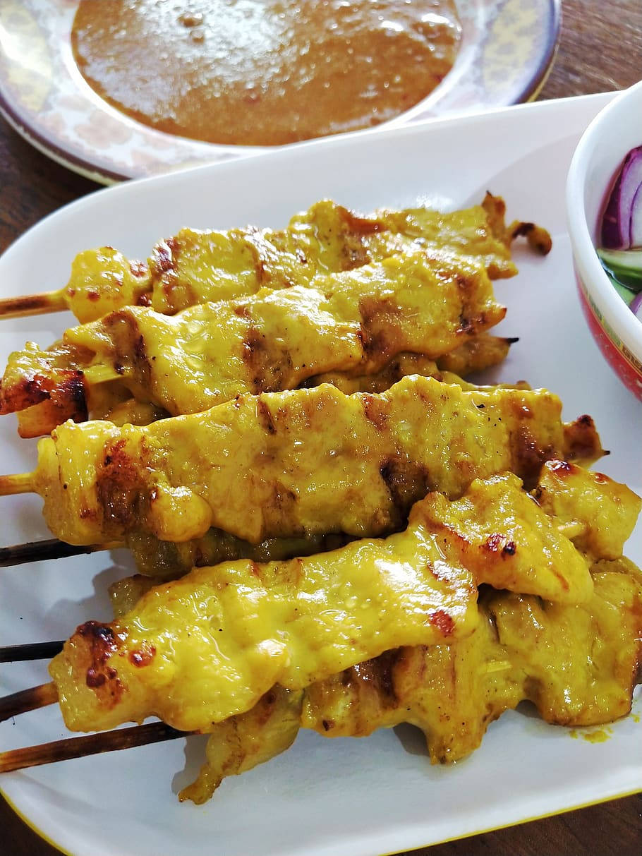 Satay 桌布 壁紙 — 金黃色的烤雞沙爹串閃爍著咖哩醬汁，旁邊放著一碗蘸醬和切片洋蔥。