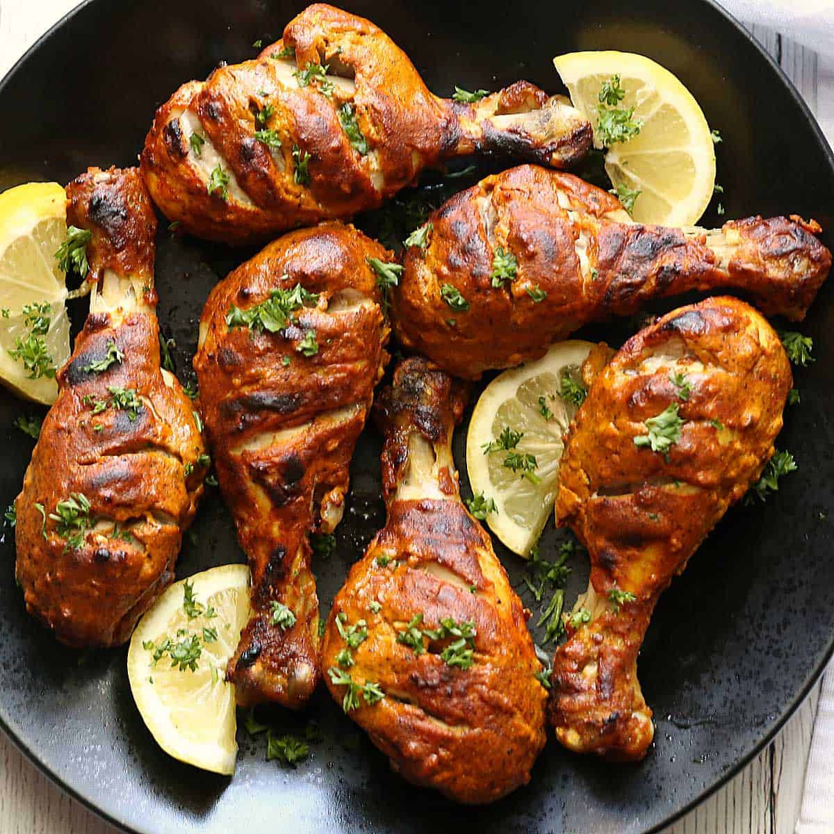Tandoori Chicken 桌布 壁紙 — 金黃色的烤雞腿，以新鮮歐芹和檸檬角裝飾，放在深色盤子上。