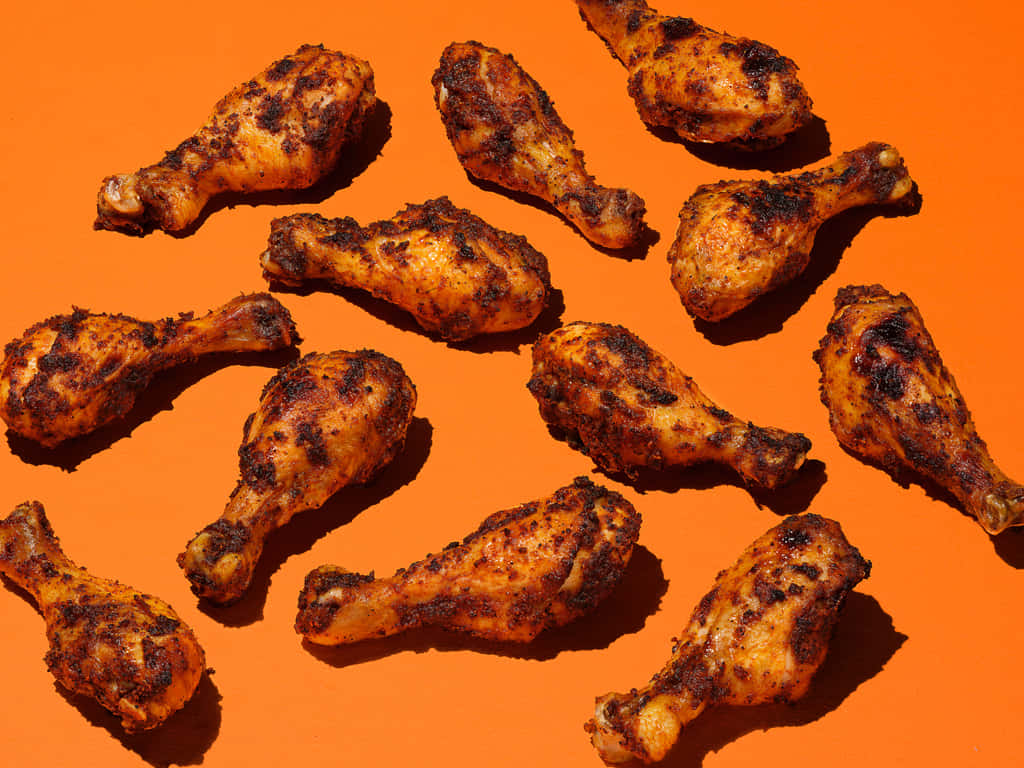 fried chicken 桌布 壁紙 — 金黃色的烤雞腿散落在鮮豔的橙色背景上，帶有強烈的陰影。