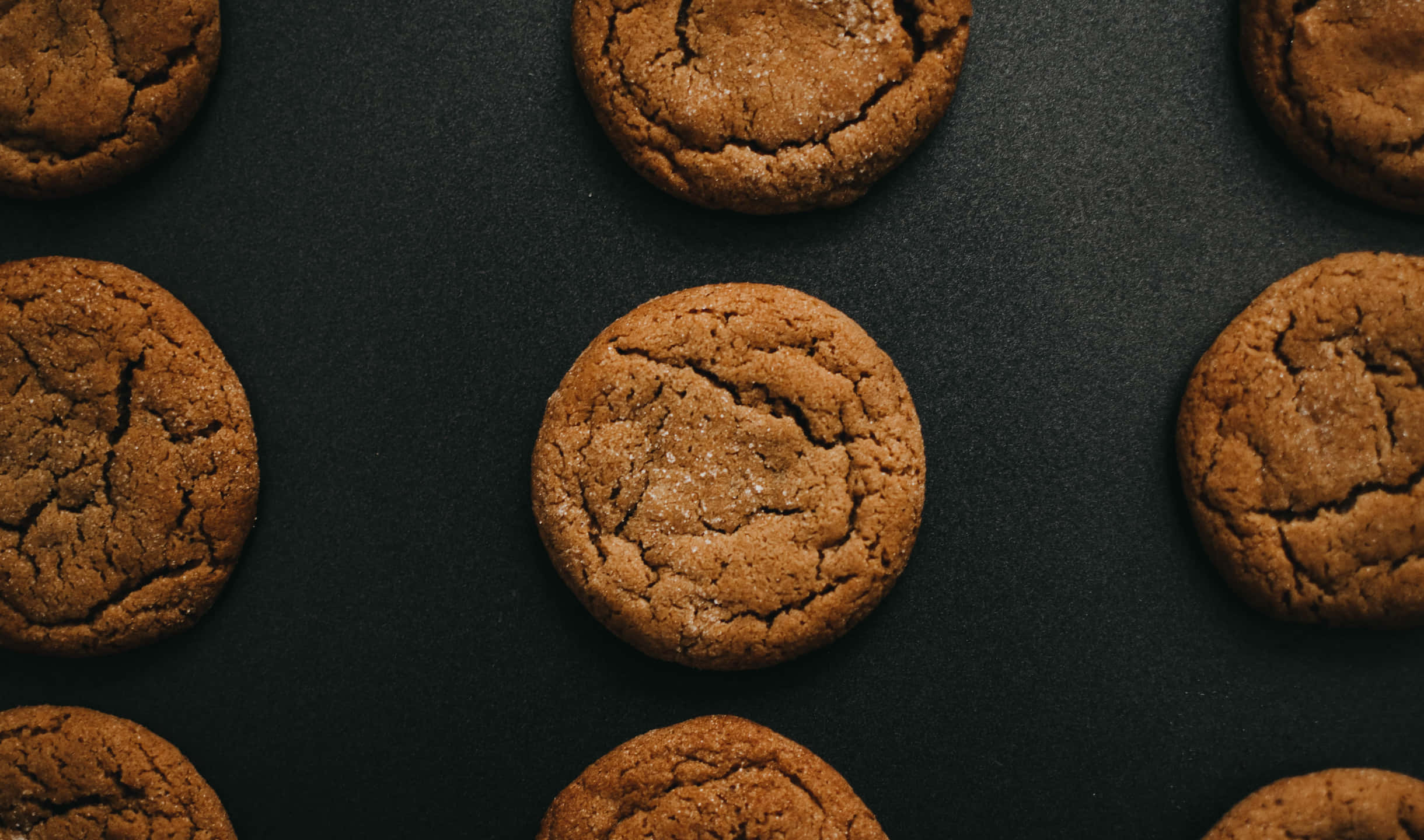 Cookies 桌布 壁紙 — 金黃色的糖餅乾，頂部有裂紋，閃閃發光的糖粒，排列在深色啞光表面上。